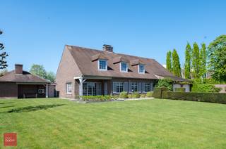 Bestaande uit inkomhal, ruime living met parket en open haard, eetplaats, ingerichte keuken met ontbijthoek, wasplaats, gelijkvloerse slaapkamer met dressing, badkamer en logeerkamer. Op het verdiep een ingerichte mancave (bar), bureelruimte, 2 slaapkamers met badkamer en een ruime zolder (eventueel extra kamers). Kelders (CV-kelder, wijnkelder, voorraad en rest kruipkelder), dubbele garage, 3-dubbele carport, overdekt terras met barbecue &amp; keuken, tuin en tuinhuis op  5.328m². Airco aanwezig. Bewoonbare opp. 652m².