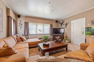 Voor meer info en foto’s, surf naar www.swevers.be – Op een ruim perceel van 865 m² in Heusden-Zolder bevindt zich deze open bebouwing met 182 m² bewoonbare oppervlakte. De woning uit 1954 biedt veel ruimte, een praktische indeling en een groene omgeving. Op het gelijkvloers vindt u een inkomhal, apart toilet, een royale woonkamer van 40,30 m² en een ruime keuken van 20,61 m² met aansluitende berging. Verder zijn er een badkamer en een ruime veranda met zicht op het achterliggende groen. De eerste verdieping telt drie slaapkamers van 20,80 m², 12,82 m² en 9,56 m². Daarnaast beschikt de woning over een kelder van 7,62 m² en een grote zolder, ideaal voor extra opslag. Het zuidwestelijk georiënteerde perceel biedt volop mogelijkheden om van de tuin te genieten. De zwemvijver en het bos achter de woning versterken het groene karakter. Een vrijstaande garage van 46 m² biedt plaats aan twee wagens en beschikt eveneens over een kelder. De kraan in de garage is aangesloten op een grondwaterput. Zonnepanelen en een batterij zijn eveneens aanwezig. Ook de ligging is praktisch, met openbaar vervoer op ca. 190 meter en winkels en restaurants op ongeveer 1 km. Scholen en ontspanningsmogelijkheden bevinden zich eveneens vlot bereikbaar. Voor meer informatie, bel 011 255 155. Bron bewoonbare oppervlakte: EPC – verslag.