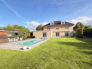 Stijlvolle villa met verwarmd zwembad en poolhouse in Tongeren 


In een rustige, residentiële wijk op wandelafstand van het centrum van Tongeren bevindt zich deze hoogwaardig afgewerkte villa uit 2008. De woning biedt een uitzonderlijke bewoonbare oppervlakte van circa 423 m² op een perceel van 13a 52ca en combineert ruimte, comfort en privacy.


Het gelijkvloers omvat een ruime inkomhal, een lichtrijke woonkamer van circa 67 m² met gashaard en grote raampartijen, en een stijlvolle keuken met eetkamer van circa 38 m². Daarnaast zijn er een praktische berging, een keukenberging en een inpandige garage.


De afzonderlijke wachtkamer en het ruime kantoor vormen een grote troef voor wie thuiswerkt of een vrij beroep uitoefent.

De woning beschikt over vijf volwaardige slaapkamers en twee badkamers. Op de tweede verdieping bevindt zich bovendien een polyvalente ruimte van circa 49 m², ideaal als speelkamer, hobbyruimte, fitness of extra bureau.


De zuidwestgerichte tuin biedt veel privacy en beschikt over een verwarmd buitenzwembad met warmtepomp van circa 48 m², ruime terrassen met elektrisch bediende zonneluifels en een ingericht poolhouse met afzonderlijke technische berging. Er is parkeergelegenheid voor drie wagens en een aparte staanplaats voor een aanhangwagen of camper.


De villa is verder uitgerust met vloerverwarming op het gelijkvloers, centrale verwarming op gas, 36 zonnepanelen, houten ramen met hoogrendementsglas en een inpandige garage met sectionale poort.


Scholen, winkels, openbaar vervoer en het centrum bevinden zich vlakbij. Ook de E313 en E40 zijn vlot bereikbaar.

Belangrijkste troeven
Circa 423 m² bewoonbare oppervlakte
Perceel van 13a 52ca
Vijf slaapkamers en twee badkamers
Kantoor met afzonderlijke wachtkamer
Polyvalente ruimte van circa 49 m²
Verwarmd zwembad met warmtepomp en ingericht poolhouse
Zuidwestgerichte tuin
36 zonnepanelen
Inpandige garage en ruime parkeermogelijkheden
Rustige ligging nabij het centrum van Tongeren


