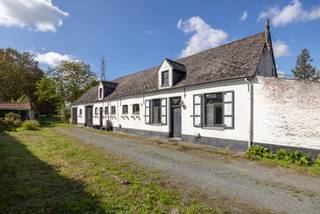 In de rustige en groene Missestraat in Duffel vinden we op nummer 64 deze charmante hoeve, gelegen tussen de centrumkernen van Duffel, Lint en Lier. Een bijzondere plek met een rijke geschiedenis, die jarenlang in handen was van dezelfde familie en vandaag klaar is voor een nieuw hoofdstuk.
De woning is toe aan renovatie, maar biedt dankzij haar ligging, oppervlakte en indeling bijzonder veel potentieel. De hoeve beschikt over bijna 300 m² bewoonbare oppervlakte en werd ingericht als tweewoonst. Het voorste gedeelte omvat een leefruimte, keuken, wasplaats, badkamer en slaapkamer. Het achterste deel beschikt over een ruime leefruimte met open keuken, badkamer, toilet en vier slaapkamers. Daarnaast zijn er twee bergruimtes met zolder, de voormalige stallen.
Het perceel waarop de woning staat heeft een oppervlakte van 1.375 m² en is gelegen in woongebied met landelijk karakter. Achteraan strekt zich maar liefst 14.241 m² landbouwgrond uit. Vandaag worden deze gronden gebruikt voor de begrazing van paarden en schapen, maar de combinatie biedt tal van mogelijkheden, steeds mits de nodige vergunningen en goedkeuringen.
Denk aan een ruime gezinswoning, kangoeroewoning, hobby- of handelsruimte, zorgboerderij, kleinschalig landbouwproject of het herstellen van de hoeve in haar oorspronkelijke glorie.
Ook qua ligging zit u hier uitstekend: rustig en groen, vlak bij de Babbelbeekse Beemden en toch met een vlotte verbinding naar Duffel, Lier, Mechelen en Antwerpen.