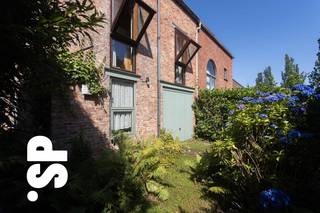 <strong>Crepain’s signatuur: een introverte blik op het moderne wonen<br /></strong>Vanaf zijn eerste realisaties hanteerde Crepain een uitgesproken persoonlijke vormentaal. De woning getuigt daarvan: een bakstenen gevel met karakteristieke vooruitgeschoven 'zichtvensters', die tegelijk sculpturaal en functioneel zijn. Achter deze eerder gesloten gevel ontvouwt zich een verrassend interieur, opgebouwd uit split-levels en loopbruggen die de binnenruimte doen aanvoelen als een gelaagd landschap. De woning benut zenitaal licht om zelfs de diepste zones tot leven te brengen — een subtiel spel van licht en schaduw, van geborgenheid en openheid.
<p><br /><strong>Een omgeving die rust en kwaliteit uitstraalt<br /></strong>De ligging van deze woning onderstreept haar stille karakter. Daarbovenop vormt Kalmthout als gemeente een van de aantrekkelijkste woonomgevingen in de regio. Niet toevallig werd Kalmthout recent uitgeroepen tot de gelukkigste gemeente van Vlaanderen<strong>. </strong>De nabijheid van het uitgestrekte natuurreservaat de Kalmthoutse Heide – op wandel- of fietsafstand – maakt deze plek bijzonder geliefd bij mensen die bewust kiezen voor een evenwicht tussen rust, natuur en bereikbaarheid. Het dorp kent een lange traditie als buitenverblijf voor Antwerpse stedelingen, net vanwege zijn unieke ligging en groene karakter. Vandaag vormt het een duurzame woonkeuze voor wie levenskwaliteit centraal stelt.</p>
<span><br /><strong>Parkzicht en privacy in balans<br /></strong>De woning geniet een bijzonder rustige ligging tegenover een publiek groenpark, wat zorgt voor een visuele ademruimte en een open uitzicht. Tegelijk garandeert het introverte karakter van het ontwerp maximale privacy — een unieke combinatie van beschutting en natuurlijke sereniteit. Achteraan sluit een wonderlijk organisch aangelegde tuin aan op de architectuur, met een speels ritme van groenstructuren en wandelpaden — een stille extensie van de woning, ontworpen om in elk seizoen te verrassen.<br /><br /><strong>Materialiteit en maatwerk<br /></strong>De gekozen materialen weerspiegelen de experimentele sfeer van de jaren ’70: zichtbeton, grenenhouten schrijnwerk, en vaste interieurelementen op maat ontworpen. Elk onderdeel — van deur tot vensterbank — draagt het stempel van een doordachte ontwerpfilosofie waarbij structuur en inrichting naadloos samenkomen.<br /><br /><strong>Over Jo Crepain (1950–2008)<br /></strong>Geboren in Brugge, opgeleid aan het Henri Van de Velde Instituut, groeide Jo Crepain uit tot een van de meest invloedrijke Belgische architecten van zijn generatie. Zijn carrière kende een vliegende start met de bekroonde woning Roels in Kapellen, nog ontworpen als student. Nadien volgden meer dan 750 projecten in binnen- en buitenland, variërend van particuliere woningen tot stedelijke herontwikkelingen. Hij was medeoprichter van het ontwerpbureau SILO en doceerde decennialang aan architectuuropleidingen in Gent, Rotterdam en Antwerpen. Zijn latere werk werd gekenmerkt door een postmoderne beeldtaal, met iconische projecten zoals de villa De Wachter in ’s Gravenwezel en het UCO-kantoor in Gent. Jo Crepain overleed in 2008, maar zijn nalatenschap leeft voort via Crepain Binst Architecture — het bureau dat hij samen met Luc Binst oprichtte.<br /><br /><strong>Een huis als ruimtelijke beleving<br /></strong>De woning aan de Voetbooglaan is een zeldzaam goed bewaard voorbeeld van Crepain’s vroege, conceptuele architectuur. Ze nodigt uit tot traag wonen, tot het ontdekken van vergezichten binnenin, en het ervaren van intimiteit zonder geslotenheid. Deze woning belichaamt de geest van een periode waarin architectuur opnieuw werd uitgevonden — helder, ruimtelijk en afgestemd op een bewuste manier van leven.<br /></span>