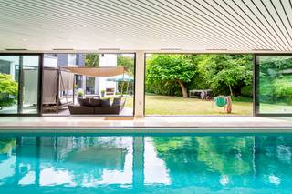 <p><span>Verken deze prachtige architectenwoning uit de jaren '70, gelegen in het gewilde Pulhof district, met een indrukwekkend bewoonbaar oppervlak van 600m². Geniet van de grandeur van een weelderig overdekt binnenzwembad op een rustig perceel van 1.400m², voor een idyllische ontsnapping in de stad zonder concessies te doen aan comfort.</span></p>
<p>Ervaar de faciliteiten van nabijgelegen scholen, winkels, speciaalzaken, gerenommeerde restaurants en supermarkten, aangevuld met de aanwezigheid van uitgestrekte groene parken - zoals het betoverende Brilschanspark. Met een indrukwekkende mobiliteitsscore van 9.5/10, kan de hele familie moeiteloos gebruikmaken van tram, bus, fietspaden, trein en snelwegverbindingen.</p>
<p><br />Bij binnenkomst verwelkomt een imposante inkomhal u, begeleid door een rijkelijke ontvangstkamer, ruime vestiaire en gastentoilet. De aanzienlijke woonruimte straalt helderheid uit dankzij de talrijke ramen met directe toegang tot het terras en de tuin. Deze geweldig ontworpen lay-out splitst zich op in aparte vertrekken voor diverse functies - met een knusse tv-kamer, comfortabele zithoeken, waarvan één met een uitnodigende open haard, en een eventueel eetgedeelte. De bijzondere charme van de ruimte wordt versterkt door de verschillende niveaus en overvloed aan natuurlijk licht; de ideale setting voor het organiseren van memorabele feestjes. Er is ook een elegante tussenverdieping met een aangename kantoorruimte die mooi aansluit op de woonkamer dankzij een vide. De volledig uitgeruste keuken toont hoogwaardige materialen, ultramoderne apparaten en een uitgebreid eiland dat comfortabel plaats biedt aan zes leden, en heeft directe toegang tot de chique eetkamer. Daarnaast vindt u het uitstekende, verwarmde zeer ruime binnenzwembad, compleet met twee kleedkamers, een doucheruimte, apart toilet en een sauna, waar overvloedige ramen nodigen schilderachtige uitzichten uit.<br /><span><br /></span>Beklim de indrukwekkende trap van roestvrij staal en glas naar de 1e verdieping, waar luxe op u wacht. U ontdekt hier een royale hoofdslaapkamer met een vaste dressing en een open badkamer, <span>voorzien van een dubbele wastafel, een tweepersoons ligbad, een inloopdouche en een apart toilet. Deze master suite biedt ook privétoegang tot de kantoorruimte. Daarnaast zijn er nog vijf andere slaapkamers, waarvan twee een grote badkamer delen met een ruime inloopdouche, dubbele wastafels en een toilet. Elke andere slaapkamer heeft een eigen aangrenzende doucheruimte. Alle slaapkamers zijn voorzien van een sierlijk koepeldak dat extra hoogte tot wel 3 meter biedt, voor een verhoogd gevoel van grandeur.<br /><span><br /></span></span>Laat u verwennen door de prachtig aangelegde tuin op het zuidwesten, naadloos verbonden met het overdekte zwembad via brede schuiframen die de grenzen tussen binnen en buiten doen vervagen en een groot terras aangevuld met elektrische zonwering en verwarmingselementen.<br /><span>Achteraan de tuin bevindt zich een ruime tuinberging voor het opbergen van al uw tuingereedschap.</span><br /><br />Deze opmerkelijke woning wordt voltooid door een riante kelder (230 m²) met boordevol opbergruimte, technische ruimtes en een authentieke 'mancave' - een paradijs voor elke gentleman.<br /><br />Ter afronding van het aanbod is er een volwaardige dubbele garage met een automatische sectionale poort, die een veilig onderkomen biedt voor uw waardevolle voertuigen.</p>
<p><span>Kortom, geniet van een zorgeloze, luxueuze levensstijl in dit betoverende, ruime verblijf dat op harmonieuze wijze de levendige sfeer van de jaren '70 combineert met moderne luxe, gelegen in het hart van een gewilde woonwijk.</span></p>
<p><br />Voor meer informatie of een bezoek aan deze prachtige woning, neem gerust contact op met Sigalit via Sigalit@reds.be of via 0475 66 84 74<br /><br /></p>