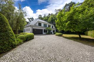 <p><span>Deze karaktervolle Vlassak-Verhulst-villa biedt een uitzonderlijke verbinding tussen architectuur, wooncomfort en natuur. De woning is prachtig gelegen in de gemeente Zoersel, op de grens met Schilde, en grenst rechtstreeks aan het indrukwekkende Driehoeksbos. De aangelegde tuin vormt hierdoor een natuurlijk verlengstuk van de leefruimtes.</span></p>
<p><span>Binnen geniet u van royale en lichtrijke leefruimtes, waarbij de open woonkamer en eetruimte via grote raampartijen rechtstreeks in verbinding staan met de tuin en terrassen. De keuken met aangrenzende tuinkamer is ideaal voor wie graag binnen en buiten laat samenvloeien.</span></p>
<p><span>Een absolute troef is de uitgebreide poolzone met zwembad op basis van zoutelektrolyse. Het ruime poolhouse beschikt over een volledig uitgeruste buitenkeuken met Braai Master, Big Green Egg, vaatwasser en koelkast. Daarnaast zijn er een sauna, buitendouche, irrigatiesysteem en grondwaterput. Een ruime fietsenberging biedt bijkomende praktische bergruimte en herbergt tevens de zwembadinstallatie.</span></p>
<p><span>Op de eerste verdieping bevinden zich vier slaapkamers. De master bedroom beschikt over een dressing en ensuite badkamer. Daarnaast zijn er nog twee bijkomende badkamers en een zolderruimte.</span></p>
<p><span>Ook op het gelijkvloers werd aandacht besteed aan comfort en functionaliteit, met een ruime inkomhal met gastentoilet en vestiaire, een praktische berging met maatkasten (voormalige garage) en een kelder.</span></p>
<p><span>De woning is uitstekend onderhouden en afgewerkt met hoogwaardige materialen zoals parket, natuursteen en maatwerkinterieurs. Het comfort wordt verder aangevuld met airconditioning, een alarmsysteem en centrale verwarming. De woning beschikt over een gunstig EPC-label B.</span></p>
<p><span>Buiten geniet u van een prachtig aangelegde, zuidgerichte tuin met volwassen groen, verschillende terrassen, optimale privacy en meerdere autostaanplaatsen.</span></p>
<p><span>Een unieke eigendom voor wie op zoek is naar ruimte, rust, privacy en een hoogwaardige woonomgeving, met het Driehoeksbos letterlijk als achtertuin.</span></p>
<p><span>Ontdek deze bijzondere villa tijdens een persoonlijke bezichtiging.</span></p>