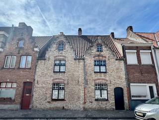 Achter deze prachtige Brugse dubbele trapgevel gelegen in het historische Onze-Lieve-Vrouwekwartier schuilt een bijzonder charmante stadswoning met een idyllische stadstuin die rechtstreeks aan de rei grenst. Deze karaktervolle woning, naar de hand van architect Hentrik Scherpereel, combineert historische charme met hedendaags wooncomfort en geniet van een uitzonderlijke ligging in het hart van de stad op wandelafstand van winkels, restaurants en het station en met een vlotte bereikbaarheid naar de uitvalswegen.
Indeling glvl.: inkomhal met gastentoilet. De gezellige leefruimte straalt warmte en authenticiteit uit dankzij de karaktervolle schouw met sfeervolle houtkachel, de prachtige balkenplafonds en de originele materialen die de woning haar tijdloze charme geven. Aansluitend bevinden zich de eetplaats met directe toegang tot de tuin, de ingerichte keuken en een praktische aanpalende wasplaats.
De absolute blikvanger van deze woning is zonder twijfel de prachtige, zonnige stadstuin met uitzicht op de rei. Deze unieke groene oase biedt een zeldzame combinatie van rust, privacy en natuur, midden in het historische hart van Brugge.
Op de 1°V zijn er twee slaapkamers, waaronder een grote master bedroom en een badkamer met inloopdouche.
De 2°V beschikt over een polyvalente ruimte die perfect kan worden ingericht als bureau, hobbyruimte of extra salon, evenals een mooie slaapkamer onder de nok. De woning is opgenomen als bouwkundig erfgoed, cv op aardgas, epc label C, asbestveilig.
Een unieke kans voor wie op zoek is naar een authentieke stadswoning op een toplocatie met een uitzonderlijke tuin aan het water.