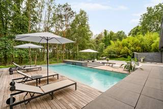 Située dans un environnement exceptionnellement calme et verdoyant, cette villa exclusive offre une combinaison unique de luxe, de confort et d'intimité. La propriété dispose de 2 à 4 chambres, d'un espace bien-être complet, d'une piscine intérieure et extérieure et de finitions de haute qualité, entièrement intégrées dans le paysage naturel.<br /><br />Rez-de-chaussée:<br /><br />Par le hall d'entrée élégant avec un grand vestiaire et des toilettes pour les invités, vous accédez aux différents espaces de vie, aux chambres au rez-de-chaussée et à l'étage.<br /><br />Lors de la conception de la maison, une attention particulière a été portée à un équilibre optimal entre l'intimité et une forte connexion avec les espaces de vie et le jardin. La cuisine centrale est le cœur de la maison et relie la salle à manger au salon. Cette cuisine de vie luxueusement équipée comprend notamment une plaque à induction avec Teppanyaki, un four, un micro-ondes, un réfrigérateur américain, des armoires à vin et une table de bar réglable en hauteur avec refroidisseur à vin intégré.<br /><br />La salle à manger et le coin salon sont élégamment séparés par une cheminée au gaz chaleureuse. De grandes baies vitrées assurent une transition fluide vers la terrasse orientée sud avec jacuzzi intégré, piscine à débordement et accès direct à la piscine intérieure au niveau -1.<br /><br />À côté se trouve une charmante salle de jardin avec sa propre cuisine, coin salon avec cheminée en bois et un grand espace repas. Un endroit idéal pour profiter de la vue sur le jardin toute l'année.<br /><br />En outre, le rez-de-chaussée dispose d'un salon supplémentaire avec cheminée en bois, qui peut être utilisé séparément grâce à des portes pivotantes élégantes.<br /><br />La suite parentale luxueuse est équipée de la climatisation, d'une cheminée au gaz et d'une télévision. La salle de bains attenante respire une élégance pure avec une grande baignoire, un double lavabo en marbre Marron Emperador, une douche à l'italienne en mosaïque de verre et des toilettes séparées. Depuis la chambre, vous avez un accès direct à la terrasse orientée est. Le dressing sur mesure avec éclairage indirect complète cet ensemble exclusif.<br /><br />La deuxième chambre dispose également de sa propre salle de bains avec double vasque et douche à l'italienne.<br /><br />À côté de la cuisine se trouve le double garage intégré. Les installations de lavage et de séchage sont discrètement intégrées dans des armoires sur mesure. Il y a également un accès à la salle des machines.<br /><br />Étage:<br /><br />L'étage est actuellement aménagé en salle de fitness professionnelle, bureau et chambre supplémentaire.<br /><br />Sous-sol:<br /><br />Le sous-sol est entièrement dédié à la détente et au bien-être. Vous y trouverez une grande piscine intérieure, un sauna et une salle de douche. La salle des machines comprend, entre autres, les installations pour la piscine, le chauffage et le système de ventilation.<br /><br />Jardin:<br /><br />Le jardin magnifiquement aménagé est un véritable paradis privé. La piscine à débordement avec cascade, douche extérieure, diverses terrasses et coins salon chaleureux font de cet espace extérieur une expérience unique. La terrasse orientée sud offre une orientation optimale au soleil et une vue magnifique sur le vert environnant.<br /><br />De plus, le jardin dispose d'un spacieux poolhouse avec douche, lavabo et toilettes.<br /><br />L'architecte a créé un jardin facile d'entretien qui s'intègre parfaitement dans le paysage naturel. Grâce à une plantation réfléchie et un éclairage d'ambiance, vous pourrez profiter ici d'une intimité maximale en toute tranquillité. Le jardin est entièrement clos du côté de la rue et ne permet aucun vis-à-vis.<br /><br />Caractéristiques:<br />*Récemment rénové (2024), nouveau toit et nouveaux sols.<br />*Équipé de panneaux solaires, installés en 2023.<br />*L'installation de chauffage de la maison et de la piscine a été renouvelée en