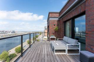 <p><b>Exclusive Penthouse Apartment with Sea Views – Entire 7th Floor</b></p>
<p>Welcome to Oosteroever, the vibrant new district of Ostend, also known as the <i>mini-Manhattan</i>. In the prestigious <b>Baelskaai 10</b> residence, you will discover an exceptional apartment where panoramic views and pure luxury come together. Completed in 2016 and designed by <b>AWG Architects</b>, this residence combines outstanding architecture, premium materials, and breathtaking views of the sea, dunes, and the Ostend skyline.</p>
<p>Upon entering, the entrance hall with separate guest toilet leads you into a bright and spacious living area, where a stunning 180° view of the city and the sea immediately captures your attention. The south-facing terrace, directly connected to the living room, allows you to enjoy a holiday atmosphere all year round. For additional comfort, the terraces are equipped with sun awnings.</p>
<p>Inside, every detail of the living space has been finished to perfection: a seamless poured floor, a built-in gas fireplace, custom-made wall cabinets, and integrated <b>Bose</b> audio. The open kitchen forms the heart of the apartment and is fully equipped with high-end appliances, including a built-in coffee machine, two refrigerators, a combi-oven, and a steam oven. Thanks to the harmoniously connected dining area and the office/hobby space, this is the perfect environment to combine living and working in style.</p>
<p>The apartment features three spacious bedrooms. The <b>master suite (28 m²)</b>, located on the east side, includes a custom-built dressing wall, an ensuite bathroom with bathtub and walk-in shower, and access to a second terrace that enjoys the morning sun. The <b>second bedroom (18 m²)</b>, located on the west side, also has its own ensuite bathroom with shower, toilet, and a sauna. From here, you have direct access to a west-facing terrace. A <b>third bedroom</b> is located at the rear of the apartment.</p>
<p>With three terraces, each offering a unique perspective – overlooking the green courtyard, the harbor, the city, and the sea – you can enjoy a different atmosphere from every angle. Practical features such as a spacious storage room and a laundry area complete this outstanding property.</p>
<p><b>Additional highlights:</b><b></b></p>
<ul>
<li><span></span>Luxurious finishes and bespoke carpentry throughout the apartment (custom-made wardrobes, natural stone, …)</li>
<li><span></span>Home automation system</li>
<li><span></span>Terraces equipped with sun awnings</li>
<li><span></span>Underfloor heating</li>
<li><span></span>Energy-efficient building with 7 floors</li>
<li><span></span>Architectural design by AWG Architects</li>
<li><span></span>Option to purchase a spacious and easily accessible underground garage box (-1)</li>
<li><span></span>Shared bicycle storage</li>
</ul>