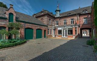 Deze neoclassicistische herenwoning anno 1868 met dubbelhuisopstand, de voormalige brouwerswoning van de brouwerij Du Bois-Haems, is gelegen in hartje Lebbeke, temidden van de driehoek Brussel-Gent-Antwerpen. Het interieur bevat talloze decoratieve elementen, waaronder een salon in Lodewijk XVI-stijl, mozaïekvloeren, stucplafonds, marmeren schouwen,...Dit pareltje heeft een parktuin van 59 are 51 ca met vijver, Lourdesgrot, antiek zwembad en talrijke imposante bomen waaronder een bruine beuk en linden. Deze indrukwekkende woning heeft een zeer ruime leefruimte (94 m²) met 3 schouwen en een leefkeuken (51 m²) met oa een AGA-fornuis, op de verdieping zijn er onder andere 7 slaapkamers en 2 badkamers. Naast de 2 garages, de wijnkelder, de paardenstallen en een gastenverblijf is er een inrijpoort met automatische poort en een met kasseien nieuw aangelegde binnenkoer. Alle technieken werden recentelijk vernieuwd (centrale verwarming op aardgas, riolering, elektriciteit), alsook de leefkeuken en de 2 badkamers met Old English douche,ligbad en wastafels. Deze woning is beschermd als monument, waardoor U kan aankopen onder het gunstig stelsel van 1% registratiekosten op voorwaarde dat de woning als gezinswoning wordt aangewend én dat er investeringen worden gedaan aan het pand. Zoniet blijft de 5%-regel gelden. Het bekomen fiscaal voordeel wordt aanzien als een fictieve subsidie, waarbij de koper binnen de vijf jaar na zijn aankoop 6% van de aankoopprijs dient te investeren in onderhouds- of renovatiewerken van het pand. Zodoende zou de nieuwe eigenaar dus 7% van de aankoopprijs betalen, zijnde 1% registratierechten en 6% aan investeringen. U kan ook daarnaast ook genieten van restauratie-en of renovatiepremies. Meer info op: https://www.onroerenderfgoed.be/nl/premies/
EPC: 400 kWh/m²/j. en UC:2070674.