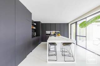 Deze uitzonderlijke <strong>villa met handelspand</strong> (momenteel ingericht als kapsalon) beschikt over een <strong>bruikbare vloeroppervlakte van ca. 352 m²</strong> en is gelegen in <strong>Mariakerke</strong> op een perceel van maar liefst <strong>1.181 m²</strong>. De woning geniet bovendien van een zuidgerichte oriëntatie.<br /><br />Het betreft een <strong>vernieuwbouw uit 2017</strong>, gerealiseerd met oog voor <strong>kwaliteit en duurzaamheid</strong>. De woning is uitgerust met aluminium ramen met dubbele beglazing, ventilatie type D, <strong>domotica</strong>, zonnescreens, <strong>vloerverwarming</strong> op zowel het gelijkvloers als de verdieping, een <strong>zonneboiler</strong> en volledig vernieuwde technieken. In 2020 werden bovendien <strong>43 zonnepanelen</strong> geplaatst. Dit resulteert in een uitstekende EPC-score van 91 kWh/m²/jaar (<strong>label A</strong>). Dit attest dateert van vóór het plaatsen van de zonnepanelen.<br /><br />De <strong>handelsruimte aan de voorzijde</strong> op het gelijkvloers is momenteel ingericht als kapsalon en heeft een oppervlakte van ca. 45 m². Deze ruimte kan perfect worden ingericht als ruimte voor een vrij beroep of praktijk, maar kan evengoed worden omgebouwd tot een inpandige dubbele garage. De nodige structuur en openingen hiervoor zijn reeds voorzien.<br /><br />Via de afzonderlijke inkomhal met gastentoilet is er toegang tot de zeer ruime woonkamer met eetplaats, die in verbinding staat met de <strong>volledig geïnstalleerde keuken</strong>. De berging/wasplaats, grenzend aan de keuken, geeft toegang tot de <strong>bijzonder ruime kelder</strong>. De woning is namelijk volledig onderkelderd. In de kelder bevinden zich aan de ene zijde de technische installaties, terwijl de andere zijde momenteel is ingericht als mancave.<br /><br />De aangelegde tuin beschikt over een <strong>overdekt terras</strong> dat volledig kan worden afgesloten, evenals een tuinhuis met carport aan de linkerzijde van het perceel.<br /><br />Op de eerste verdieping bevinden zich de <strong>masterbedroom met dressing</strong>, twee kinderkamers met een afzonderlijke badkamer, een logeerkamer, een bureauruimte (die als 5de slaapkamer kan dienen) en een tweede badkamer met ligbad en douche.<br /><br />Wenst u zelf de vele kwaliteiten en troeven van deze unieke villa te ontdekken? Neem dan contact op met Theo voor een bezoek ter plaatse via theo@convas.be.