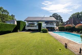 <p><strong>Exclusieve split-levelvilla met 5 slaapkamers, zwembad en prachtig aangelegde tuin</strong></p>
<p>Wie op zoek is naar een woning met <strong>karakter</strong>, <strong>uitzonderlijke volumes</strong> en een <strong>unieke woonbeleving</strong>, zal onmiddellijk gecharmeerd zijn door deze <strong>indrukwekkende split-levelvilla</strong>. Dankzij haar <strong>speelse architectuur</strong>, <strong>royale leefruimtes</strong> en <strong>prachtige buitenomgeving</strong> biedt deze eigendom een <strong>zeldzame combinatie van luxe, comfort en functionaliteit</strong>.</p>
<p>Vanaf het eerste moment valt de <strong>bijzondere indeling</strong> van de woning op. De verschillende niveaus creëren een natuurlijke scheiding tussen wonen, slapen, werken en ontspannen, terwijl de open verbindingen zorgen voor een aangenaam gevoel van <strong>ruimte en licht</strong>. <strong>Grote raampartijen</strong> laten het daglicht overvloedig binnenstromen en bieden op verschillende plaatsen een prachtig zicht op de tuin en de omliggende <strong>groene omgeving</strong>.</p>
<p>Het absolute middelpunt van de woning is zonder twijfel de <strong>uitzonderlijk ruime woonkamer</strong> van maar liefst circa <strong>83 m²</strong>. Dankzij de directe toegang tot het <strong>ruime terras</strong> vloeien <strong>binnen- en buitenleven</strong> naadloos in elkaar over.</p>
<p>Een niveau hoger bevindt zich de <strong>ruime leefkeuken</strong> die perfect aansluit op de aangename eetruimte. Deze combinatie vormt het <strong>kloppende hart van het huis</strong> waar koken, tafelen en samenzijn centraal staan.</p>
<p>De villa telt maar liefst <strong>vijf volwaardige slaapkamers</strong>, verspreid over verschillende niveaus. Hierdoor geniet ieder gezinslid van voldoende <strong>privacy en comfort</strong>. De <strong>hoofdslaapkamer van circa 33 m²</strong> vormt een echte <strong>privésuite</strong> met een royaal gevoel van ruimte en rust.</p>
<p>Verder beschikt de woning over een <strong>ruime badkamer</strong> met ligbad en douche, meerdere sanitaire voorzieningen en een afzonderlijke wasruimte, wat het dagelijkse comfort aanzienlijk verhoogt.</p>
<p>Voor wie van thuis uit werkt of extra ruimte nodig heeft voor een praktijk, hobby of creatieve activiteiten, biedt de woning een <strong>uitzonderlijk ruime kantoorruimte</strong> van ongeveer <strong>31 m²</strong>.</p>
<p>Buiten ontvouwt zich een ware <strong>oase van rust en privacy</strong>. De <strong>grote, perfect onderhouden tuin</strong> vormt een groene omgeving waar jong en oud het hele jaar door kunnen genieten. Centraal in de tuin ligt het <strong>zwembad</strong>, dat tijdens de zomermaanden garant staat voor <strong>ontspanning</strong> en een echt <strong>vakantiegevoel in eigen huis</strong>. De verschillende terrassen rond de woning bieden op elk moment van de dag een aangename plek om te genieten van de zon of de schaduw.</p>
<p>De architectuur van deze split-levelvilla zorgt niet alleen voor een bijzonder ruimtelijk gevoel, maar geeft de woning ook een <strong>unieke uitstraling</strong> die haar onderscheidt van klassieke villa's.</p>
<p><strong>Troeven op een rij</strong></p>
<p>✔ Exclusieve split-levelarchitectuur<br />✔ 5 ruime slaapkamers<br />✔ Ruime kantoorruimte<br />✔ Verschillende terrassen<br />✔ Grote zolder met uitbreidingsmogelijkheden<br />✔ Perfect onderhouden en aangelegde tuin<br />✔ Verwarmd zwembad<br />✔ Veel natuurlijke lichtinval</p>
<p><strong>Een bezoek zal u zonder twijfel overtuigen van de uitzonderlijke kwaliteiten van deze eigendom.</strong></p>