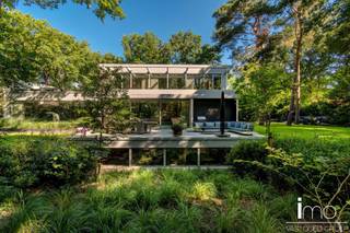 Instapklare high-end villa in meer- en golfomgeving.<br /><br />Deze modernistische woning met unieke invulling biedt alle comfort en rust in een oase van groen en bos.<br /><br />Bij het betreden van dit pand worden we meteen verbaasd door de dakramen naast de woonkamer en de aandacht voor bijzondere, exclusieve materialen. De leefruimte is voorzien van een mooie gashaard en wordt door een kastenwand gescheiden van de bureau-ruimte. Aansluitend is er een eetplaats met geweldige wijnkast, alsook een volledig uitgeruste keuken met speciale kookapparatuur.<br /><br />Naadloos weggewerkt in de keukenwand vinden we een deur die toegang biedt tot de gelijkvloerse slaapkamer met eigen badkamer, de berging en wasplaats met koelcel en gelijkvloerse staanplaats voor de wagen.<br />De woning biedt alle moderne comfort en werd uitgerust met de nieuwste technieken waaronder alle voorbereidingen om een lift te kunnen installeren. Door de gebruikte technieken is de woning natuurlijk ook energiezuinig. (E50)<br /><br />Op de eerste verdieping vinden we een ruime master-bedroom met eigen haard die 180° zicht biedt over de aangelegde tuin. Hierbij werd zowel een bad als douche voorzien met op het dakterras tevens een stoomcabine en whirlpool. Naast de badkamer vinden we een inloopdressing met indirecte verlichting en lichtkoepel voor overdag.<br /><br />Behalve het bijzondere leefconcept met rijkelijke lichtinval overal op de bovengrondse verdiepingen, heeft de woning nog een ruime kelder dewelke langs binnen en met een autolift langs buiten toegankelijk is. Deze ruimte van 350 m2 kan aangewend worden tot een enorm atelier of een bijzondere stalplaats voor een prachtige autocollectie. Andere invullingen zijn natuurlijk ook mogelijk gezien er natuurlijk licht binnenvalt en er ook op de ondergrondse verdieping ramen voorzien zijn.<br /><br />Bekijk ook zeker onze website voor de interactieve grondplannen.<br />Meer info via Jean.Heylen@imovastgoed.be of via 015/34.34.54.