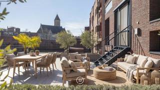 Achter de gevel van Residentie Mondriaan schuilt een bijzonder ruim appartement waar de buitenruimte meteen de toon zet. Een royaal, zuidgericht dakterras van 100 m², groen aangelegd met niet-woekerende bamboe, olijfbomen en lavendel, met charmant open zicht op de kerktoren.<br /><br />Gelegen in een kleinschalige residentie beschikt het appartement over een bruto bewoonbare oppervlakte van circa 185 m² en is volledig instapklaar. De voorgevel verwijst subtiel naar het werk van kunstschilder Piet Mondriaan en geeft het gebouw een herkenbare signatuur.<br /><br />Bij aankomst brengt de privétoegang via de lift u rechtstreeks in het appartement. Ingebouwd kastwerk bij de lift zorgt voor een verzorgde en praktische ontvangst. Van daaruit opent het geheel zich naar een ruime leefruimte, waar licht, volume en rust samenkomen.<br /><br />De doorlopende eiken parketvloer, het witte maatwerk en de kwaliteitsdeuren zorgen voor een rustig interieur. Brede raampartijen met hoogrendementsglas brengen het daglicht rijkelijk binnen en versterken het ruimtelijke gevoel. Eetruimte, salon en bureauruimte vormen samen één open leefomgeving, met het royale terras als natuurlijk verlengstuk. In de leefruimte is bovendien de mogelijkheid voorzien om een gashaard aan te sluiten. <br /><br />De keuken sluit volledig aan op de leefruimte en is strak opgevat met wandkasten, een kookeiland met een werkblad van maar liefst 5 m, ingewerkte lades en ingebouwde toestellen van onder meer Smeg en Siemens. <br /><br />Het terras vormt de uitgesproken meerwaarde van dit appartement. Door de oppervlakte, de zuidgerichte oriëntatie en de groenaanleg ontstaat een buitenruimte die verder gaat dan een klassiek terras. De antislip terrastegels, lavendel, niet-woekerende bamboe, olijfbomen, stroomaansluitingen en automatische bewatering maken deze plek geschikt voor dagelijks gebruik, lange avonden buiten en genieten van alle rust en gezelligheid. <br /><br />Het slaapgedeelte is apart ingedeeld. Beide slaapkamers beschikken over een eigen badkamer met wastafelmeubel en inloopdouche. De master heeft daarnaast een ligbad, ingebouwde maatkasten en toegang tot een afzonderlijk balkon. Beide slaapkamers zijn voorzien van extra comfort, waaronder airco of warmtebron en tv-aansluiting. Ook aan praktische details werd gedacht, zoals vliegenramen.<br /><br />Technisch is het appartement optimaal en zorgvuldig uitgerust met automatische screens, ventilatie type C die zich automatisch aanpast, brandalarm, jaarlijks gecontroleerde brandbeveiliging, een Viessmann-gasketel en een berging met aansluitingen voor wasmachine en droogkast.<br /><br />Verder beschikt het appartement over EPC-label A met een energiescore van 84 kWh/m² jaar. <br /><br />Ondergronds is een privatieve staanplaats inbegrepen.<br /><br />Een bijzonder ruim en energiezuinig appartement met een royale private buitenruimte die de woonbeleving hier op een uitzonderlijke manier versterkt.