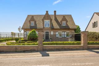 Gelegen op een uitzonderlijke locatie waar rust en open vergezichten samenkomen, onderscheidt deze standingvolle villa zich als een zeldzame opportuniteit voor wie op zoek is naar een verfijnde levensstijl met ruimte, comfort en ontwikkelingspotentieel. Bij binnenkomst wordt u verwelkomd in een elegante inkomhal die leidt naar ruime leefruimtes badend in natuurlijk licht. De royale leefruimte, met brede openingen naar zowel de voor- als achtertuin, creëert een warme en lichtrijke sfeer. Deze sluit naadloos aan op een grote, zorgvuldig ingerichte keuken, aangevuld met een praktische bijkeuken, waarin esthetiek en functionaliteit perfect samenkomen. Op het gelijkvloers bevindt zich bovendien een volwaardige slaapkamer, ideaal voor dagelijks gebruik of het ontvangen van gasten. Op de verdieping beschikt de nachtruimte over drie comfortabele slaapkamers en een ruime badkamer uitgerust met een douche, een ligbad en dubbele wastafels. De ruime overloop biedt tal van inrichtingsmogelijkheden, zoals een stijlvolle bureau of een multifunctionele ruimte. De zolderverdieping, volledig ingericht in 2026, opent nieuwe perspectieven met twee extra kamers en een tussenruimte, die volledige vrijheid bieden voor het creëren van privé-suites, werkruimtes of andere indelingen naar wens.<br /><br />Buiten komt de villa volledig tot haar recht. Een groot zuidwestgericht terras nodigt uit tot ontspanning en biedt een prachtig uitzicht over de omliggende velden, met een uniek panorama dat met de seizoenen mee evolueert. Een volledig uitgeruste barbecuezone maakt dit gezellige geheel compleet, ideaal voor aangename momenten met familie en vrienden. Een deel van het terrein werd doordacht afgescheiden om ruimte te creëren voor dieren, een moestuin of andere projecten naar wens, en biedt zo extra ontwikkelingsmogelijkheden. De volledig onderkelderde woning verhoogt de aantrekkingskracht verder met een ruime garage, veel bergruimte, een praktische wasruimte en een zeer grote polyvalente ruimte die kan worden ingericht als speelkamer, hobbyruimte of atelier, met de mogelijkheid tot het voorzien van een extra badkamer en minibar. Daarnaast is er ook een fitnessruimte met douche aanwezig voor optimaal wooncomfort. De villa is uitgerust met PVC-ramen met dubbele beglazing en beschikt over een modern verwarmingssysteem met een condenserende gaswandketel, wat garant staat voor energie-efficiëntie en dagelijks comfort. Gebouwd in 1979 en zorgvuldig gerenoveerd in 1998 en 2024, werd deze eigendom steeds perfect onderhouden. Het is meer dan een woning; het is een echte levensstijl, waarbij elk detail werd doordacht om een uitzonderlijke woonomgeving te bieden. Bent u op zoek naar een ruime woning, ideaal gelegen en met tal van mogelijkheden? Dan kan deze villa wel eens uw toekomstige thuis worden.