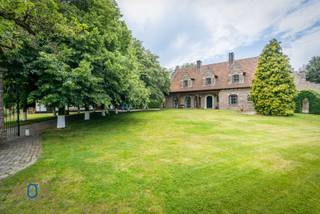 Compleet onttrokken aan de massa verschuilt dit landhuis met bijgebouwen in Engelse stijl zich in de geborgenheid & privacy van de eigen parktuin (7.222 m2). Deze omvat oa meerdere terrassen, zwemvijver met ponton, paviljoen, idyllische boomhut, Bbq, waterput, fruitboomgaarden, ... De lange opritlaan geflankeerd door een knappe lindenbomenrij zet onmiddellijk de toon bij het betreden van deze unieke architecturale eigendom met bekoorlijke binnen- en buitenomgeving. Het KLOEKE & ROBUUSTE profileert zich naadloos door het gebruik van zeer kwalitatieve materialen zoals natuursteen, veel maatwerk, houtwerk zoals oa deuren & trappen vervaardigd uit volle eik, lambrisering, balken voor de gaanderij en plafonds, verwarming met tegelkachels ...<br /><br />Het gelijkvloers hoofdwoning verdeelt zich in:<br />* Statige inkomhal met vestiaire & gastentoilet<br />* Leefruimte met eet- en zitkamer voorzien van een tegelkachel <br />* Volledig geïnstalleerde woonkeuken eveneens met een knappe tegelkachel met fornuis voorzien<br />* Bureel / slaapkamer<br />* Berging - wasruimte met extra pantry<br />* Gastenverblijf met leefruimte en bar voorzien van pelletkachel & slaapkamer op verdieping<br />* Feeëriek aangelegde parktuin met achterliggende vijver, boomhut & paviljoen<br /><br />Het bijgebouw bestaat uit:<br />* Garage & carport bijgaand met zeer ruime parking<br />* Atelierruimte met extra vliering<br /><br />Via de knappe eiken trap bereiken we de 1ste VD die omvat:<br />* Zeer ruime nachthal met zithoek<br />* 4 slaapkamers waarvan 1 met directe toegang tot de ensuite badkamer (hoekbad - wastafel)<br />* 1 badkamer (dubbele wastafel - inloopdouche - ligbad - toilet)<br /><br />De dakverdieping herbergt nog een zolderruimte die bereikbaar is via een uitschuifbare trap.<br /><br />EXTRA TROEVEN: Riant woonvolume / Meerdere bestemmingsmogelijkheden (B&B - Woon- werkcombinatie - Kangoeroewoning) / Exclusieve parktuin / Veel parkeergelegenheid / Volledige privacy /...