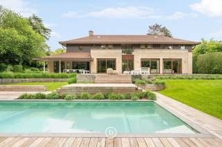 Ontdek deze exclusieve villa in het gegeerde Domein van Bouchout te Wemmel, gelegen op een prachtig perceel van circa 25 are met optimale privacy. De woning, gebouwd in 2001, beschikt over een fraai aangelegd terras met een verwarmd buitenzwembad en geniet van een rustige, groene omgeving. Binnen werd gekozen voor hoogwaardige, duurzame materialen en uitgebreid maatwerk, wat resulteert in een stijlvolle en tijdloze afwerking. Dankzij het gunstige EPC-label B combineert deze eigendom exclusief wooncomfort met energiezuinigheid. Verder beschikt de villa over een inpandige garage, een ruime kelder met wijnkelder en meerdere buitenstaanplaatsen.<br /><br />De woning met een bewoonbare oppervlakte van 526 m2 is als volgt ingedeeld: <br /><br />0: Ruime inkomhal met gastentoilet, met in de linkervleugel een afzonderlijk bureau, een elegante ontvangstruimte met open haard en een gezellige tv-kamer. De rechtervleugel omvat een ruime eetkamer die aansluit op de volledig uitgeruste keuken met kwalitatieve afwerking. Aansluitend bevindt zich een praktische bijkeuken met wasruimte en veel ingebouwde opbergruimte, rechtstreeks verbonden met de garage. Op het gelijkvloers is bovendien een polyvalente kamer aanwezig die kan dienen als eerste slaapkamer of gastenkamer.<br /><br />+1: Op de eerste verdieping bevindt zich een ruime masterbedroom met dressing en een aansluitende badkamer, uitgerust met ligbad, douche, toilet en dubbel wasmeubel. De masterbedroom is bovendien voorzien van airconditioning. In de nachthal zijn er nog twee badkamers, waarvan één met ligbad en één met douche. Daarnaast zijn er drie ruime kinderkamers, elk afgewerkt met maatwerk en praktische inbouwoplossingen.