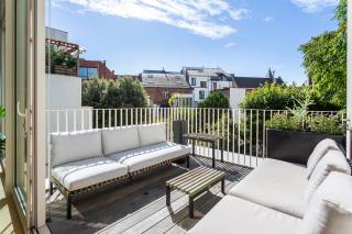 Achter de authentieke gevel van dit herenhuis bevindt zich op de eerste verdieping een stijlvol appartement, gelegen in de Belegstraat, op een gegeerde locatie die het bruisende Zuid en de geliefde Markgravebuurt met elkaar verbindt. Vanuit deze centrale ligging bevinden gezellige koffiebars, restaurants en lokale handelszaken zich op wandelafstand, net als de Troonplaats, de Amerikalei en het KMSKA. Ook het stadscentrum en de belangrijkste invalswegen zijn vlot bereikbaar.<br /><br />Via de inkomhal, voorzien van ingemaakte kasten, betreedt u de royale leefruimte. Dankzij de volledig beglaasde achterzijde geniet deze aangename ruimte van een overvloed aan natuurlijk licht. De parketvloer en moderne gashaard zorgen voor een warme en verfijnde sfeer. De leefruimte sluit naadloos aan op de open keuken met royaal kookeiland, die als centraal element van de woning fungeert. De keuken werd uitgerust met een hoogwaardige selectie Miele-toestellen, waaronder een steamer en wijnkoeler, en wordt vervolledigd door een Quooker. Aansluitend bevindt zich een praktische berging met aansluitingen voor wasmachine en droogkast, ideaal voor extra voorraad en opbergruimte.<br /><br />Vanuit de leefruimte heeft u rechtstreeks toegang tot het aangename, zuidgerichte terras. Het zicht op de Sint-Michielskerk en de omliggende tuinen zorgt bovendien voor een bijzonder groen en rustig kader, midden in de stad.<br /><br />De masterbedroom bevindt zich aan de voorzijde van het appartement en geeft uit op een charmant Frans balkon. De kamer beschikt over een volledige wand aan ingemaakte kasten, goed voor een zee aan opbergruimte. Daarnaast bevindt zich een tweede volwaardige slaapkamer, eveneens voorzien van ingemaakte kasten en flexibel in te richten als kinderkamer of bureau.<br /><br />De smaakvolle badkamer werd afgewerkt met hoogwaardige materialen, waaronder natuursteen en Vola-kranen. Een ruime inloopdouche met infraroodfunctie, dubbele wastafel en vrijstaand ligbad creëren hier een luxueuze en comfortabele ruimte.<br /><br />Tot slot beschikt het appartement over een private kelderberging, inbegrepen in de prijs. Een inpandige autostaanplaats is bij aan te kopen voor € 45.000.<br /><br />Interesse in deze parel?<br />Contacteer LISTED voor een bezoek: +32 3 283 51 51.