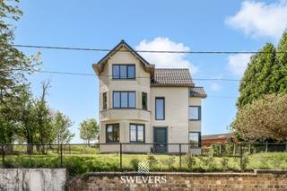 Voor meer info en foto’s, surf naar www.swevers.be –<br /><br />In het charmante gehucht Lauw, deelgemeente van Tongeren, vind je deze statige open bebouwing uit 1947 te Donkelstraat 52 op een perceel van 8are45ca. De woning werd in 2022 grondig gerenoveerd met behoud van karaktervolle elementen en biedt modern wooncomfort in een groene omgeving. Met een bewoonbare oppervlakte van 235 m² is dit de ideale gezinswoning, perfect ook voor thuiswerkers of hobbyisten.<br /><br />De lichtrijke leefruimte van 29,8 m² geeft via grote raampartijen uitzicht op de achterliggende weilanden. De keuken van 26,9 m² is strak ingericht en voorzien van een kookeiland, hoogwaardige toestellen en directe toegang tot het zuidgerichte terras—perfect voor zomerse avonden.<br /><br />Er zijn vier volwaardige slaapkamers (15, 14,4, 12,3 en 12,2 m²), waarvan de master bedroom is uitgerust met een riante inloopdressing van 12,2 m². Twee luxueuze badkamers (16 en 14,32 m²) bieden alle comfort, inclusief bad, inloopdouche en dubbele wastafels. Een extra gastentoilet is eveneens aanwezig.<br /><br />Praktisch scoort de woning sterk dankzij de ruime kelder met meerdere bergingen en een perceel van 8a45 met voldoende parkeergelegenheid. Een vergunning voor een carport is reeds verkregen. Duurzaamheid komt aan bod via een regenwaterput van 10.000 liter.<br /><br />De witgrijs gekaleide gevel en het tijdloze interieur met warme materialen creëren een hedendaagse, sfeervolle woonstijl. Dankzij de zuidgerichte oriëntatie geniet je hier van maximale lichtinval en zonovergoten buitenmomenten.<br /><br />Voor meer informatie, bel 012 699 900. Bron bewoonbare oppervlakte: EPC – verslag.