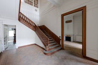 <p>Aan de Frankrijklei staat dit statige herenhuis met een verfijnde lijstgevel, sierlijke smeedijzeren balkons en een leien mansardedak met ronde dakvensters.</p>
<p>Een adembenemende inkomhal met dubbele plafondhoogte. Een brede eikenhouten trap met sierlijk gedraaide balusters en een fraai gebeeldhouwde trappaal leidt, langs een lambrisering in massief hout, naar de bovenverdiepingen. De vloer is afgewerkt met visgraatparket. Hoog boven de trap vangt een monumentaal glas-in-loodraam het licht: een negentiende-eeuws pronkstuk. Rijk gestucte plafonds en kroonlijsten versterken het karakter van het eigendom.</p>
<p>Vanuit de hal geeft een dubbel openslaande deur toegang tot een lichtrijk salon, waar een verfijnde marmeren haardmantel met een sierlijke overschouw de blikvanger vormt. Het visgraatparket, de hoge plafonds en de verzorgde lambrisering zetten de sfeer van de inkomhal verder door op de gelijkvloerse verdieping.<br />Het pand telt 6 ruime slaapkamers en 3 badkamers, verspreid over de bovenverdiepingen. De overloop op de eerste verdieping vormt een verlengstuk van de inkomhal: een statige ruimte met witte lambriseringen en hetzelfde prachtige glas-in-loodraam. Boven de traphal zorgt een glazen lichtstraat, met zicht op de balustrade van de bovenverdieping, voor een verrassende lichtinval tot diep in het huis.</p>
<p>Achteraan opent het huis zich op een verrassend groene stadstuin – een zeldzaamheid voor een pand aan de Leien. Een gietijzeren balustrade in Belle Époque-stijl siert het terras aan de achtergevel waarbij een buitentrap naar de tuin afdaalt. <br />Achteraan de tuin ligt het koetshuis: een sfeervol tuinpaviljoen. Vandaag leent dit karaktervolle bijgebouw zich uitstekend als atelier, kantoor aan huis of gastenverblijf.</p>
<p>Het pand is volledig onderkelderd, wat bijkomende bergruimte en technische mogelijkheden biedt.</p>
<p>De Frankrijklei maakt deel uit van de Leien, de negentiende-eeuwse boulevards rond de historische Antwerpse binnenstad. Zeer centraal gelegen nabij Botanische tuin, Theaterplein en het Zuid.</p>
