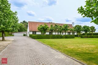 Landhuis bestaande uit inkomhal, zeer ruime living met open haard, eetplaats, ingerichte keuken met ontbijthoek, gelijkvloerse slaapkamer met badkamer, ruim bureel (of hobbykamer), wasplaats en berging. 3 Slaapkamers, dressing en badkamer op verdiep. Tuin met bijgebouw (bar) en ruime garage/opslagruimte. 14 zonnepanelen aanwezig. Opp. 4.190m²<br />