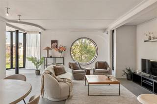 <p>In New York noemen ze het park-front living. Aan de Vlaamsekaai 26 krijg je de Antwerpse versie: een architecturaal hoekappartement op de derde verdieping, met het Zuidpark letterlijk als voortuin.<br />Hier zijn het vooral de ramen die het verschil maken. Grote glaspartijen, een karaktervolle erker en de iconische ronde ramen trekken het daglicht binnen en kaderen het park en de stad vanuit verschillende hoeken. Groen in de zomer, warme kleuren in de herfst en altijd zicht op het leven op het Zuid.</p><p>- Hoekappartement met veel natuurlijk licht<br />- Frontaal en zijdelings zicht over het Zuidpark<br />- Bijzondere architectuur met ronde ramen en erker<br />- Lift<br />- Private kelderberging met aansluiting voor wasmachine en droogkast<br />- Kleinschalig gebouw<br />- Toplocatie tegenover het Zuidpark</p><p>De leefruimte is open, licht en allesbehalve standaard. De ronde maatkeuken in warm hout vormt het architecturale middelpunt en sluit naadloos aan op de eet- en woonkamer. De erker creëert dan weer een aparte plek om te lezen, werken of simpelweg naar het park te kijken.</p><p>De slaapkamer beschikt over ingemaakte kasten. Aansluitend vind je de badkamer met wastafel en ligbad met douchefunctie. Een apart gastentoilet en de private kelderberging maken het praktisch compleet.</p><p>En buiten? KMSKA, Zuidpark, Scheldekaaien, restaurants, koffiebars en galeries liggen allemaal binnen wandelafstand. De auto mag hier gerust wat vaker blijven staan.<br />New York heeft Central Park. Antwerpen heeft het Zuidpark. Hier zit je op de eerste rij.</p><p>Benieuwd naar het uitzicht achter die ronde ramen? Plan je bezoek via Sinjoor.be of bel 03 283 05 00.</p>