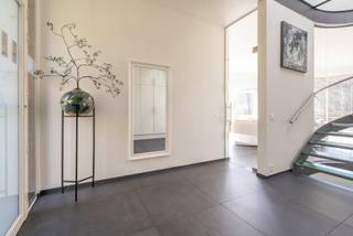 <p>Wonen in harmonie met de natuur. Deze unieke, recent geactualiseerde woning is ontworpen om het prachtige bosgebied en de vijver naadloos te integreren in uw dagelijks leven. Met een overvloed aan natuurlijk licht en vier comfortabele slaapkamers biedt deze woning een oase van rust en sereniteit. Ontsnap aan de drukte en omarm de schoonheid van uw eigen privédomein.<br /><br />De woning is ontworpen door het gekende Architectenbureau Luc Denis uit Antwerpen. De natuurlijke vijver en het omringende bos was voor de architect aanleiding een hoofverblijf met een ronde vorm te creëren met daaraan een rechthoekige uitbouw met de ruimtes die aanvullend aan de woonfunctie zijn. <br /><br />De woning is toegankelijk via de centrale inkomhal. De inkomhal is voorzien van een spiltrap uitgevoerd met transparante treden. Door de dakkoepel in het zinken dak treedt het licht hier op een subtiele manier binnen. Aan de rechterzijde de eerste kamer. Oorspronkelijk ontworpen als atelier maar uitstekend bruikbaar als slaapkamer of thuiskantoor. Deze ruimte heeft een eigen uitgang naar buiten. Daarnaast een vestiairekast, toegang tot het gastentoilet en de kelder.<br /><br />De kelder is via een vaste trap bereikbaar. In de kelder, met een oppervlakte van ca. 24m², de nutsvoorzieningen en de omvormer met batterijen voor de zonnenstroominstallatie.<br /><br />De trap geeft toegang tot de cirkelvormige verdieping. Op de verdieping 2 badkamers, 3 ruime slaapkamers en een ruime was-, en strijkruimte. De badkamers voorzien van toilet en inloopdouche. De hoofdbadkamer voorzien van een zogenaamd Japans toilet.<br /><br />Terug naar het gelijkvloers. Via de glazen deur toegang tot de leefruimte met eethoek, zithoek en tv-hoek. Totaal oppervlakte ca. 70m². Aansluitend de veranda met een oppervlakte van ca. 21m². De veranda is door een glaspartij afgesloten van de tv-hoek en heeft volledig zicht over de vijver en het achterliggende bos. De tv-hoek kent een hoofdzakelijk dichte wand waardoor een besloten sfeer wordt gecreëerd, De zithoek kijkt uit over het houten terras en de vijver naar het achterliggende bos. De waardevolle moerascipres (Taxodium distichum) is een parel aan de rand van de vijver en geeft in de zomer een aangename filtering van de zon met behoud van het licht. Aan de zithoek de eethoek en aansluitend de keuken. <br /><br />De eethoek meet ca. 24m², de keuken is volledig nieuw en heeft een moderne uitstraling. Vanuit de keuken toegang tot 2 bergingen van ca. 6 en 12m². In de achterste berging bevindt zich ook de verwarmingsinstallatie. De woning wordt verwarmd door middel van een condenserende HR-ketel op gas en heeft op het gehele gelijkvloers vloerverwarming. Terug naar de keuken toegang tot de extra badkamer met toilet en de deur naar de dubbele carport. De carport heeft een oppervlakte van ca. 36m². De woning is voorzien van een centraal stofafzuigsysteem.<br /><br />Op het dak 29 zonnepanelen van elk 405Wp geplaatst in 4 strings voor maximale opbrengst. De zonnepanelen gekoppeld aan 6 accu’s met een totale opslagcapaciteit van 20kWh. Aan de carportzijde is een laadpaal geplaatst voor het opladen van de elektrische wagens. De EPC-waarde is een uitstekende waarde voor de woning maar is nog niet aangepast met deze wijzigingen en de woning zal dus nog een stuk beter resultaat laten zien.<br /><br />Recent is er een extra overkapping gebouwd met een oppervlakte van ca. 33m². Vanaf de veranda is de woning voorzien van een houten terras met aansluitend een loopbrug. In de tuin wordt op korte termijn nog een complete louncheruimte opgericht.</p>
<p>De tuin en de vijver zijn goed onderhouden en de woning is instapkaart. Benieuwd naar deze bijzondere woning in de groene en rustgevende omgeving van Kalmthout? Bel gerust voor een uitgebreid bezoek. Via 03 240 11 99 is een afspraak snel gemaakt.</p>