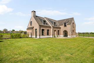 Deze stijlvolle woning is gebouwd in 2020 en is afgewerkt met kwalitatieve en duurzame materialen. Deze eigendom beschikt over een sfeervolle woonkamer, lichte leefkeuken, wasplaats, 4 slaapkamers op de 1e verdieping, bureau of 5e slaapkamer op de gelijkvloerse verdieping, badkamer, 2e nog af te werken badkamer, dressing en dubbele carport met overdekt terras. <br />De villa is gelegen op een groen domein met vrij uitzicht op omliggende weilanden. Hier geniet u van ruimte en rust op een interessante locatie vlakbij de Nederlandse grens. <br /><br />Gelijkvloers:<br />U betreedt de woning via de ruime inkomhal met apart toilet. Hierlangs heeft u toegang tot de sfeervolle woonkamer op tegelparket dat via de grote ramen achteraan uitzicht geeft op de open tuin. De moderne leefkeuken met groot eiland en natuurstenen werkblad is voorzien van kwalitatieve toestellen (inductievuur, combi oven/micro, oven, warmhoudlade, vaatwasmachine, koelkast). De wasplaats is toegankelijk via een ingewerkte deur in de keuken wat voor een strak geheel zorgt. Vooraan de woning bevindt er zich nog een bureauruimte of extra gelijkvloerse slaapkamer afgewerkt met een prachtige visgraatparkettegel.<br /><br />Eerste verdieping:<br />De bovenverdieping is eveneens uitgerust met parket en is opgedeeld in 4 slaapkamers waarvan de masterbedroom voorzien is van een dressing en eigen badkamer. Verder bevindt er zich nog een afzonderlijk toilet en tweede badkamer die nog verder naar eigen smaak af te werken is. <br /><br />Tuin:<br />In de tuin is het aangenaam vertoeven door het weidse uitzicht. De tuin is voorzien van een ruim bijgebouw waar plaats is voor meerdere wagens en ook gebruikt kan worden als overdekt terras. Doordat het perceel ca. 6.886m² is, bestaat de mogelijkheid dieren te houden.<br /><br />Bijzonderheden:<br />- Ruim perceel met open zichten<br />- Instaklare woning met kwalitatieve afwerking<br />- Regenwaterput aangesloten op toiletten en wasmachine <br />- 2 geboorde grondwaterputten van 12m diepte<br />- Energiezuinige woning (E30) met zonnepanelen en vloerverwarming <br />- Alarm en domotica