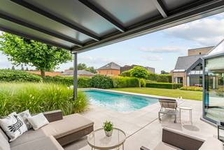 Cette spacieuse maison familiale avec 4 chambres, 2 salles de bains, poolhouse et piscine est située dans une rue calme à environ 2,5 kilomètres du marché de Geel sur un terrain de 1 091 m². La maison comprend au rez-de-chaussée un hall d'entrée avec toilettes invités et vestiaire, bureau, salon, salle à manger, cuisine, cellier, cave et un garage. À l'étage, une chambre principale avec dressing et salle de bains, une chambre avec salle de bains attenante, 2 chambres, un grand palier, des toilettes sur le palier. De plus, un grenier spacieux d'environ 40 m². A l'extérieur, un jardin magnifiquement aménagé avec piscine et un poolhouse d'environ 105 m² avec garage intégré.<br /><br />Disposition :<br />Rez-de-chaussée :<br />Vous entrez dans la maison par un hall d'entrée central avec des toilettes invités et un vestiaire. De là, vous avez accès d'une part à un bureau au rez-de-chaussée et d'autre part à l'espace de vie. Le bureau est complètement séparé des espaces de vie privés, ce qui le rend également idéal pour l'exercice d'une profession libérale. L'espace de vie est divisé en un coin salon confortable avec cheminée et une salle à manger lumineuse à l'arrière de la maison. Au centre se trouve également un bureau aménagé. Adjacente à la salle à manger, vous trouverez une cuisine équipée avec coin petit déjeuner baigné de soleil. La cuisine est équipée de tout le confort moderne et dispose d'un micro-ondes, d'un four à air chaud, d'un réfrigérateur, de plaques de cuisson, d'une hotte et d'un lave-vaisselle. De chaque côté de la cuisine, vous bénéficiez d'un espace de stockage pratique sous la forme d'une cave d'environ 10m² et d'une buanderie/chaufferie équipée. De plus, un garage spacieux avec porte automatique. Celui-ci est en connexion avec le hall d'entrée et la buanderie.<br /><br />Étage :<br />Par un escalier central, vous accédez à l'étage. Ici, vous arrivez sur un grand palier avec des toilettes séparées. À votre droite, vous trouverez les deux premières chambres. À votre gauche, un palier donnant sur une troisième chambre sur parquet avec salle de bains attenante, équipée d'une douche à l'italienne et d'un double lavabo. Cette salle de bains est également accessible depuis le palier et peut être fermée à la chambre. À l'arrière du palier, vous trouverez à l'avant de la maison une grande chambre principale sur parquet. Cette chambre est adjacente à un dressing aménagé, des toilettes séparées et une belle salle de bains avec douche, baignoire indépendante et 2 lavabos.<br /><br />Grenier :<br />Au deuxième étage, vous trouverez une grande pièce mansardée d'environ 45 m² divisée en 2 pièces. La première était autrefois utilisée comme salle de jeux, la partie arrière sert de débarras. Vous trouverez également des installations sanitaires (eau chaude et froide avec évier).<br /><br />Aménagement du jardin :<br />Adjacent au salon et à la salle à manger, vous trouverez une terrasse ensoleillée et une terrasse couverte accessible de l'intérieur par 2 baies vitrées. Le jardin est également magnifiquement aménagé avec pelouse et parterres de verdure. À l'arrière, vous trouverez une piscine chauffée avec volet roulant automatique et un spacieux poolhouse avec terrasses attenantes. Le poolhouse dispose d'un grand espace de vie, de sanitaires (douche et toilettes), d'une kitchenette et d'un garage intégré avec porte automatique. De plus, un espace cave pratique pour tous vos outils de jardin.<br /><br />Caractéristiques exceptionnelles :<br />* Emplacement calme et verdoyant avec vue dégagée à proximité du centre de Geel<br />* Bon score énergétique de 199 kWh<br />* Surface habitable généreuse de 471 m²