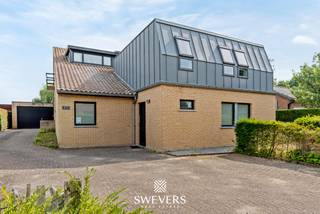 Voor meer info en foto’s, surf naar www.swevers.be – Ontdek deze uitzonderlijk ruime kangoeroewoning op een perceel van 19a 67ca in het gegeerde Kuringerheide, vlak bij Hasselt en natuurgebied De Platwijers. De woning werd gebouwd in 1980 en in 2006 functioneel omgevormd tot een volwaardige kangoeroewoning. Met een bewoonbare oppervlakte van 337 m², een gunstig EPC-label B en een praktische indeling is dit de ideale thuis voor grote gezinnen, inwonende familie of wie wonen en zorg wil combineren. De hoofdwoning beschikt over een lichtrijke leefruimte, keuken, bureau, slaapkamer en badkamer op het gelijkvloers. Op de verdieping bevinden zich meerdere slaapkamers, waardoor de woning in totaal zeven slaapkamers telt. Daarnaast zijn er drie badkamers aanwezig. De aparte woonunit beschikt over een eigen inkomhal, leefruimte met keuken, slaapkamer en badkamer, zodat privacy en zelfstandigheid verzekerd zijn. Onder de volledige woning bevindt zich een ruime kelder van 88 m², ideaal als opslag-, hobby- of werkruimte. Buiten geniet u van een dubbele carport, een zuidgerichte tuin en een heerlijk zwembad waar u in alle rust kan ontspannen. Airconditioning en rookdetectoren zorgen voor extra comfort. De woning biedt bovendien alle mogelijkheden om ze verder naar eigen smaak te moderniseren. Dankzij de rustige ligging bevinden scholen, winkels, openbaar vervoer en het centrum van Hasselt zich op korte afstand, terwijl ook de autosnelwegen vlot bereikbaar zijn. Een unieke eigendom met veel ruimte, flexibiliteit en toekomstmogelijkheden. Voor meer informatie, bel 011 255 155. Bron bewoonbare oppervlakte: EPC – verslag.
