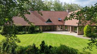 Bij het betreden van deze zeer goed onderhouden en instapklare stijlvolle villa wordt u verwelkomd in een indrukwekkende, lichtrijke inkomhal met gastentoilet en praktische vestiairekast. Via een elegante glazen deur komt u in de ruime leefruimte en eetkamer, waar grote raampartijen een fraai uitzicht bieden op de prachtig aangelegde volgroeide tuin en mooie bomen. De sfeervolle leefruimte beschikt bovendien over een open haard, stijlvolle bar, de ideale plek om in alle gezelligheid te genieten van een aperitief.<br /><br />Aansluitend bevindt zich aan de ene zijde een afzonderlijk bureau met maatwerkkasten, perfect voor thuiswerk of een professionele activiteit. Aan de andere zijde vindt u de comfortabele master suite op het gelijkvloers, bestaande uit een dressing, badkamer, boudoir en ruime slaapkamer, dit alles voorzien voor levenslang wooncomfort. Vanuit de dressing biedt een zolderluik toegang tot de ruime zolderverdieping van maar liefst 39 m² met hoge plafondhoogte die, indien gewenst, als leef- of werkruimte bij de woning betrokken kan worden.<br /><br />De volledig uitgeruste keuken geniet eveneens van een mooi zicht op de tuin en vormt het hart van de woning. Naast de keuken bevindt zich een tweede bureau en een extra polyvalente ruimte -momenteel ingericht als koele berging- die, indien gewenst, eenvoudig kan worden geïntegreerd om de keuken verder uit te breiden. Verder beschikt het gelijkvloers over een praktische wasplaats met afzonderlijke inkom, een dubbele garage met automatische poort en een aangrenzende werkplaats/atelier.<br /><br />Op de verdieping bevinden zich drie volwaardige slaapkamers. De eerste slaapkamer beschikt over een eigen sauna en douchecel. De tweede, bijzonder ruime kamer biedt tal van mogelijkheden en kan desgewenst ingericht worden als zelfstandige studio (conciërge, nanny of kangoeroewoning), aangezien de nodige aansluitingen voor een keuken en/of badkamer reeds aanwezig zijn. De derde slaapkamer is uitgerust met een eigen douchekamer en extra bergruimte.<br /><br />Ook buiten weet deze villa te imponeren. Het riante terras van 54 m² is uitgerust met tal van comfortvoorzieningen, waaronder een overdekt gedeelte, terrasverwarming, zonnetent, zonnescreens en een ingebouwde barbecue. Dankzij de gunstige zuidoostoriëntatie geniet u hier de hele dag van de zon in alle rust en privacy.<br /><br />Bovendien bestaat de mogelijkheid om de prachtig aangelegde naastgelegen tuin afzonderlijk aan te kopen. Dit perceel betreft een bouwgrond van 1.848 m² met een straatbreedte van circa 35 meter. Meer informatie en prijs op aanvraag via frederik@immovdl.be.<br /><br />Deze eigendom onderscheidt zich verder door haar uitstekende ligging in een residentiële en groene omgeving, op fietsafstand van zowel het centrum van Schilde als Sint-Antonius. Extra troeven zijn het alarmsysteem, zonnewering, de rolluiken, de vloerverwarming op het gelijkvloers, de rolstoelvriendelijke indeling met brede deuren en de grondwaterput met automatisch sproeisysteem (momenteel niet functioneel). Ook de grote private parking aan de zijkant van woning en de grote houtberging, die discreet in de tuin geplaatst is zijn absolute troeven van de woning.<br /><br />Een uitzonderlijke woning waar ruimte, comfort en een prachtige en rustige, groene omgeving harmonieus samenkomen.