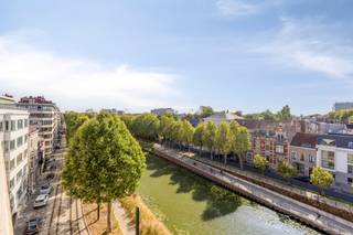 Op een unieke locatie aan de Coupure vinden we dit bijzonder lichtrijke appartement met een vve troef die je maar zelden tegenkomt: maar liefst 100 m² terras, verdeeld over een voor- en achterterras. Voeg daar de vergezichten over het water, de stad en de historische skyline van Gent aan toe, en je krijgt een plek die meer aanvoelt als een penthouse dan als een klassiek appartement.<br /><br />Het appartement beschikt over ca. 100 m² bruto bewoonbare oppervlakte en geniet dankzij de grote raampartijen van bijzonder veel lichtinval. De leefruimte vormt het hart van de woning en staat rechtstreeks in verbinding met de terrassen. <br /><br />De aparte keuken is praktisch ingericht en kan, indien gewenst, eenvoudig worden opengewerkt naar de leefruimte. Verder zijn er twee slaapkamers, een badkamer en voldoende bergruimte. Op het terras bevinden zich bovendien nog twee compacte bergingen en in de kelder is een private berging van ca. 4 m² aanwezig.<br /><br />Het appartement dateert van 1994 en is goed onderhouden. Wie vandaag kiest voor een modernere afwerking, kan met een gerichte update het geheel volledig naar eigen smaak brengen. Technisch staat het appartement alvast sterk: het beschikt over een EPC-label B en is asbestveilig. Er werd recent ook een airco/ warmtepomp voorzien in de leefruimte. <br /><br />En dan zijn er natuurlijk de terrassen. Samen goed voor ongeveer 100 m² buitenruimte bieden ze verschillende mogelijkheden: ontbijten in de ochtendzon, lang tafelen met vrienden, een groene stadstuin op hoogte creëren of simpelweg genieten van de rust en het uitzicht. De buitenruimte maakt van dit appartement iets wat je niet zomaar in vier muren kunt vatten.<br /><br />Verder is er een ondergrondse staanplaats aanwezig die mee aangekocht dient te worden voor 40.000 EUR. <br /><br />Een appartement met ruimte, licht en vooral een uitzonderlijke ligging met de Coupure voor de deur en het historisch centrum van Gent als panorama.<br /><br /><br />Bestuursmaatregelen in het maatregelenregister: nee