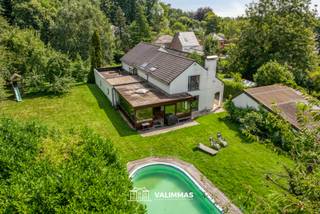 VALIMMAS verkoopt deze zeer ruime alleenstaande woning, met prachtige en ideaal georiënteerde tuin, op ± 38 are...
Het gelijkvloers bestaat uit een inkomhal, een toilet, een bureel (±44m², thans in twee aparte burelen/kamers verdeeld), een grote living (± 54m²) met open haard, een veranda/leefruimte (± 42m²), een volledig ingebouwde keuken met bijkeuken/wasplaats, en een garage voor twee wagens.
De verdieping herbergt een overloop/nachthal met inbouwkasten, een toilet, een master bedroom (± 30m²) met uitzicht op de tuin, drie mooie slaapkamers, een badkamer met ligbad en inloopdouche, en een badkamer met douche.
Achteraan, in een apart bijgebouw, zit een atelier/hobbyruimte (± 35m² + zolder) en een tuinberging met de pomp/filterinstallatie van het zwembad (± 9 x 4m). Rondom ligt een prachtig aangelegde tuin met gazon, terras, bomen, sieraanplantingen, hagen....
Achterin gelegen woning op groot perceel in residentiële buurt Oude Baan/Brukersebaan, met gemakkelijke verbindingen naar Aalst, Ternat, Asse, E40, diverse KMO-zones, …