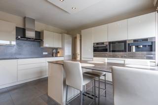 <p>Deze ruime villa uit 1980 biedt een mooie combinatie van wonen, ontspanning en tal van extra mogelijkheden. Aan de voorzijde beschikt de woning over een mooie voortuin. Links naast de woning bevindt zich het zwembad met aansluitend een ruim terras en poolhouse met douche. Achter de woning is er bovendien een groot terras.</p><p>Op het gelijkvloers beschikt de woning over een ruime inkomhal, aparte bureauruimte, toilet, ingerichte keuken met bijkeuken en aansluitende berging, een eetplaats in een ruime L-vormige leefruimte. Dankzij het grote schuifraam staat de leefruimte rechtstreeks in verbinding met het terras en de buitenruimte.</p><p></p><p>De eerste verdieping omvat een nachthal, badkamer met ligbad, douche en dubbele wastafel en vijf ruime kamers. Deze kunnen naar eigen behoefte worden ingericht als slaapkamers, bureau, hobbyruimte of fitnessruimte.</p><p><strong>Een absolute troef is de grote loods onder de woning.</strong> Deze beschikt over drie hoge inrijpoorten, een interne laadkade en frigo- en koelinstallaties. De loods biedt heel wat mogelijkheden voor een zelfstandige activiteit, opslag, werkplaats of hobby. Ook voor liefhebbers van oldtimers, verzamelaars of wie meerdere voertuigen wil stallen, is dit een bijzonder interessante ruimte.</p><p></p><p>De loods is bereikbaar via de oprit rechts van de woning via de Oude Geraardsbergsebaan, <strong>Daarnaast is er een tweede, vlottere toegang tot de loods rechtstreeks vanaf de Ninoofsesteenweg</strong>, via het afzonderlijke perceel bouwgrond. Dit perceel, inclusief deze toegang, kan apart worden aangekocht. Hierdoor beschikt de loods over een bijzonder praktische ontsluiting, ook voor grotere voertuigen of vrachtwagens. Dit maakt het geheel onder meer interessant voor een zelfstandige activiteit, opslag, een werkplaats of het stallen van voertuigen en oldtimers.</p><p></p><p>Een veelzijdig eigendom voor wie op zoek is naar een ruime woning en grote buitenruimte, gecombineerd met een uitzonderlijke loods en tal van mogelijkheden.</p><p></p><p><strong>EPC: label C – 266 kWh/m²/jaar</strong></p>