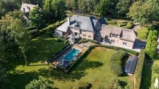 <strong>Deze indrukwekkende en uitzonderlijk ruime villa combineert luxe, comfort en veelzijdigheid op een bijzonder hoog niveau. De woning is ontworpen voor wie exclusief wil wonen en tegelijk waarde hecht aan ontspanning, privacy en representatieve ontvangstmogelijkheden. Gelegen op een royaal perceel van maar liefst 6.420 m² en met een indrukwekkende bewoonbare oppervlakte van 1.047 m². Hoogwaardige materialen, doordachte indelingen en een uitzonderlijk aanbod aan faciliteiten – waaronder een verwarmd buitenzwembad, wellness en een volledig ingericht privé-café – maken van deze villa een unieke eigendom.<br /></strong><span><br />Gelijkvloerse verdieping</span>: U betreedt de villa via de imposante inkomhal met stijlvolle trap naar de verdiepingen en een gastentoilet. Vanuit deze centrale hal heeft u toegang tot de verschillende leefruimtes.<br /><br />Aan de linker voorzijde van de woning bevindt zich een royale bureel- of hobbykamer, die eveneens bereikbaar is via een aparte zij-ingang. Deze ruimte leent zich uitermate goed voor thuiswerk, een zelfstandige activiteit of een afzonderlijke woon- of leefruimte.<br /><br />Aan de achterzijde van de villa bevindt zich de zeer ruime leefkeuken, badend in natuurlijk licht dankzij de grote raampartijen met directe verbinding naar de terrassen en de tuin. De keuken is ingericht met een hoogwaardige Siematic-opstelling, een royaal werkeiland en een uitgebreide semi-professionele uitrusting, bestaande uit onder meer: 2 vaatwassers, Teppanyaki-plaat, 2 inductiekookplaten, gasvuur, grote oven, stoomoven, extra oven met warmhoudlade, ijsmachine en 2 diepvriezers. Een absolute eyecatcher is de indrukwekkende, geklimatiseerde wijnwand met glazen deuren.<br /><br />Aansluitend aan de keuken bevinden zich meerdere leefruimtes, waaronder een salon, een gezellige zithoek en een aparte televisiekamer. Elke ruimte heeft haar eigen sfeer, maar samen vormen ze een harmonieus en luxueus geheel.<br /><br /><span>Soutterain:</span> De volledig ingerichte ondergrondse verdieping biedt tal van multifunctionele mogelijkheden. Hier vindt u een professioneel uitgeruste fitnessruimte met rechtstreekse toegang naar buiten, evenals een ingebouwde sauna. Daarnaast beschikt deze verdieping over een ruim en sfeervol ingericht privé-café, dat dankzij de rechtstreekse verbinding met de garage ook perfect kan dienen als feest-, ontvangst- of eventruimte.<br /><br /><span>Eerste verdieping:</span> De ruime nachthal geeft toegang tot de royale masterbedroom, voorzien van een aangrenzende dressing en een luxueuze badkamer met ligbad, inloopdouche, dubbele wastafel en toilet. Verder bevinden zich op deze verdieping nog 3 volwaardige slaapkamers, elk voorzien van een eigen badkamer. <br /><br /><span>Tweede verdieping</span>: Deze verdieping beschikt over<strong> </strong>twee ruime slaapkamers die samen gebruikmaken van een gedeelde badkamer.<br /><br /><span>Buitengebeuren:</span> De villa is gelegen op een ruim, volledig aangelegd perceel met maximale privacy. Het verwarmde buitenzwembad vormt het centrale element van de tuin en wordt omringd door meerdere zonneterrassen. Zowel overdekte als open terrassen sluiten naadloos aan bij de woning en zijn ideaal georiënteerd om op elk moment van de dag van de zon te genieten. <br /><br /><span>Bijzonderheden:</span> <br />- Volledige renovatie in 2009<br />- Domotica (Gira)<br />- Multi-room audio systeem <br />- Alarmsysteem met camerabewaking <br />- Natuurleien dak en deel rieten dak <br />- Volledig onderkelderd met multifunctionele ruimtes<br />- Ideaal voor grote gezinnen<br />- Inpandige garage voor meerdere wagens (tot vier) en rechtstreeks toegankelijk vanuit de woning