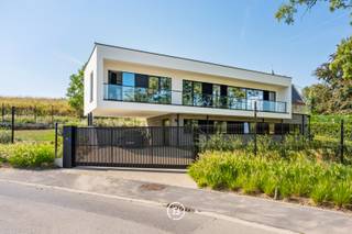 Op een uitzonderlijke locatie aan de voet van de Kanarieberg, met het Muziekbos als indrukwekkend decor, bevindt zich deze recente designvilla uit 2023. De combinatie van hedendaagse architectuur, hoogwaardige afwerking en een panoramisch uitzicht over het omliggende landschap maakt van deze eigendom een bijzonder geheel.<br /><br />De woning werd ontworpen rond licht en openheid. Grote raampartijen brengen het landschap maximaal naar binnen en zorgen voor een voortdurende verbinding met de omgeving. De strakke architectuur wordt daarbij verzacht door een warme en luxueuze interieurafwerking, waardoor een eigentijdse maar aangename woonomgeving ontstaat.<br /><br />Het gelijkvloers is ingericht als private slaap- en werkzone, met drie slaapkamers, een ruime masterbedroom met maatwerkkasten en dressing, een hoogwaardige badkamer en een afzonderlijke bureauruimte. De verdieping vormt het sociale hart van de woning, met een ruime open leefruimte waarin keuken, eetplaats en zithoek harmonieus samenkomen. Vanuit hier geniet men niet alleen van een uitzonderlijke hoeveelheid natuurlijk licht, maar vooral van het continue zicht op het Muziekbos.<br /><br />Het buitenleven sluit hier naadloos op aan. Het ruime terras met luifel en het bijkomende zonneterras bieden verschillende plaatsen om te genieten van de rust en het landschap. De aangelegde tuin, dubbele carport en automatische schuifpoort zorgen voor het nodige comfort en privacy.<br /><br />Ook op energetisch en technisch vlak werd de woning volledig afgestemd op hedendaags wooncomfort, met onder meer een warmtepomp, vloerverwarming, 48 zonnepanelen, een dubbele thuisbatterij, regenwaterrecuperatie, camerabewaking en een laadpaal. Met een EPC-label A combineert de villa haar luxueuze uitstraling met een bijzonder energiezuinig karakter.<br /><br />Een eigendom voor wie hedendaagse architectuur weet te waarderen, maar vooral op zoek is naar een woning met een bijzondere ligging, rust en een uitzicht dat elke dag opnieuw blijft verrassen.