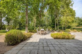 <p>In een doodlopende straat in 's-Gravenwezel bevindt zich deze tijdloze villa op een uitzonderlijk mooi perceel van meer dan 5.000 m² met een straatbreedte van circa 60 meter. De woning grenst rechtstreeks aan een uitgestrekt parkgebied en ligt op wandelafstand van de slotgracht van het Kasteel van ’s-Gravenwezel. Een unieke combinatie van absolute rust, privacy en een vlotte bereikbaarheid naar Antwerpen en de omliggende gemeenten.</p>
<p><strong>GELIJKVLOERS<br /></strong>Riante inkomhal 28 m² op blauwe hardsteen met eiken parket. Aansluitend bevindt zich een gastentoilet met handenwasser en een tweede halgedeelte met trap.</p>
<p>Het bureel van 22 m² met aparte ontvangstruimte leent zich perfect voor comfortabel thuiswerk.</p>
<p>Daarnaast is er een sfeervolle bibliotheek van 13 m² met ingemaakte boekenkast.</p>
<p>De imposante leefruimte van 122 m² op brede eiken parketvloer beschikt over een kastenwand en een inbouwhaard en geniet van een prachtig zicht op de tuin. De eetkamer bevindt zich in een orangerie met haardvuur en grote ramen die uitgeven op het terras en de parktuin.</p>
<p>De landelijke keuken van 25 m² met werkblad in blauwe hardsteen sluit aan op een charmante tuinkamer op parket, eveneens met directe toegang tot de tuin.</p>
<p>Verder op het gelijkvloers bevinden zich een garage van 29 m² en een kelder van 14 m². Het aangelegde terras van 30 m² en de volledig omheinde, fraai aangelegde tuin versterken het gevoel van ruimte en privacy.</p>
<p>Bijkomend is er een eiken bijgebouw met twee overdekte autostaanplaatsen en een afgesloten garage.</p>
<p><strong>Verdieping<br /></strong>De nachthal van 15 m² is afgewerkt met sisal-tapijt.<br />De royale masterbedroom van 56 m² beschikt over een eigen salon, dressing en ensuite badkamer. Daarnaast zijn er 3 bijkomende slaapkamers van 13 m², 13 m² en 17 m².<br />Eveneens is er een aparte strijk- en wasruimte van 12 m² met ingemaakte ladekasten en aansluiting voor wasmachine en droogkast.<br />De 2de badkamer van 11 m² is afgewerkt in natuursteen en uitgerust met lavabo, ligbad en toilet.</p>
<p>Via een vlizotrap bereikt u de zolder van 32 m².</p>
<p><strong>BIJZONDERHEDEN<br /></strong>Cv op aardgas, dubbele beglazing, houten schrijnwerk, alarminstallatie, waterontharder, parlofoon, dimmers, ingebouwde spots, 2 open haarden, tuinverlichting, volledig omheinde tuin met automatische toegangspoort.</p>
<p><strong>POSITIEVE PUNTEN<br /></strong>Absolute toplocatie<br />Gelegen in doodlopende straat<br />Prachtig aangelegde tuin met oprijlaan<br />Rechtstreekse aansluiting op natuur- en parkgebied</p>