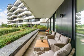 Voor meer info en foto’s, surf naar www.swevers.be – Dit instapklare gelijkvloerse appartement ligt aan de achterzijde van residentie Zuidzicht op Scheepvaartlaan 48/0.05 in Hasselt. Dankzij deze rustige ligging geniet u van zicht op de binnentuin en een glimp van het Albertkanaal. Het appartement werd gebouwd in 2016, is bereikbaar met de lift en biedt een bewoonbare oppervlakte van 74,38 m². De indeling bestaat uit een inkomhal, twee slaapkamers, een badkamer en een ruime leefruimte met open keuken. De woonkamer en keuken vormen samen een aangename leefzone met veel licht en directe toegang tot het overdekte terras van maar liefst 30 m². Dit terras is een grote troef en voelt aan als een verlengstuk van de leefruimte. De hoofdslaapkamer is volwaardig ingericht, terwijl de tweede kamer perfect dienst kan doen als bureau, kinderkamer, logeerkamer of dressing. De badkamer beschikt over een ligbad met douchescherm en een ruime wastafel. Met EPC-score B is het appartement bovendien energiezuinig. Het pand is momenteel verhuurd aan 890 euro per maand, plus 125 euro gemeenschappelijke kosten, wat het ook interessant maakt als investering. Een ondergrondse autostaanplaats kan optioneel aangekocht worden voor 32.500 euro. Dankzij de ligging nabij het centrum van Hasselt bevinden winkels, horeca, ontspanning, scholen, openbaar vervoer en de autosnelweg zich allemaal vlot bereikbaar. Voor meer informatie, bel 011 255 155. Bron bewoonbare oppervlakte: EPC – verslag.