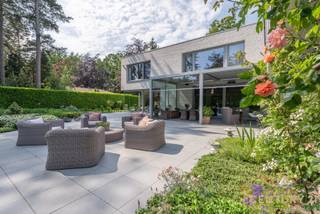 <h3>Exclusieve architectenvilla op toplocatie in villawijk De Lint</h3>
<p>Op een prachtig zuidwestgericht perceel, op wandelafstand van het unieke natuurgebied De Liereman, bevindt zich deze hedendaagse en onder architectuur gebouwde villa. Deze uitzonderlijke woning combineert tijdloze architectuur, royale leefruimtes en een hoogwaardig afwerkingsniveau met een uitstekende bereikbaarheid. Zowel Eindhoven als Antwerpen bevinden zich op slechts ca. 25 minuten rijden, waardoor u geniet van het beste van twee werelden: rust, natuur en een vlotte verbinding.</p>
<p>Bij aankomst wordt u verwelkomd in een ruime inkomhal met vestiaire en gastentoilet. Via stijlvolle dubbele deuren betreedt u de indrukwekkende woonkamer, waar de grote raampartijen een panoramisch zicht bieden op de prachtig aangelegde tuin. Het overvloedige natuurlijke licht en de fraaie tuinzichten creëren een unieke woonbeleving. Aansluitend bevindt zich een open ruimte die perfect dienst kan doen als bureau of leeshoek, open van karakter maar toch afzonderlijk van de leefruimte.</p>
<p>De sfeervolle doorkijkhaard vormt een elegante verbinding tussen de woonkamer en de royale leefkeuken. Deze keuken verkeert in perfecte staat van onderhoud, is uitgerust met kwalitatieve toestellen, beschikt over een groot werkblad en biedt plaats aan een ruime eettafel. Dankzij de grote schuiframen loopt binnen naadloos over in buiten. Achter de keuken bevinden zich een praktische bijkeuken en een aparte wasruimte. De inpandige dubbele garage met automatische poort en personenlift vervolledigt het comfort op het gelijkvloers.</p>
<p>Op de verdieping geeft de royale nachthal toegang tot de indrukwekkende master suite met inloopdressing en een luxueuze badkamer. Daarnaast zijn er nog twee volwaardige slaapkamers met een gedeelde badkamer. De ruime studiekamer kan eenvoudig worden ingericht als vierde slaapkamer en beschikt bovendien over een eigen terras.</p>
<p>Ook buiten weet deze villa te imponeren. De volgroeide, volledig omheinde tuin biedt optimale privacy en vormt een waar groen paradijs. Meerdere zonneterrassen en een overdekt terras nodigen uit om in alle seizoenen van het buitenleven te genieten. Het extra losstaande garagegebouw biedt bijkomende mogelijkheden voor wagenliefhebbers, hobbyruimte of extra opslag.</p>
<p>Naast het uitzonderlijke wooncomfort onderscheidt deze villa zich door haar onderhoudsvriendelijke karakter. Dankzij de duurzame aluminium raamprofielen en de kwalitatieve gevels in gevelsteen zijn er geen schilderwerken aan het buitenschrijnwerk of de buitenmuren nodig, wat resulteert in een stijlvolle uitstraling met een minimum aan onderhoud.<br /><br /><strong>Een uitzonderlijke villa voor wie ruimte, comfort, privacy, kwaliteit en een onderhoudsarme woonomgeving weet te waarderen.</strong></p>
<h3>Troeven van deze woning</h3>
<ul>
<li>Wandelafstand van natuurgebied De Liereman</li>
<li>Zuidwestgericht perceel met optimale bezonning</li>
<li>Personenlift naar de verdieping</li>
<li>Vloerverwarming op gelijkvloers én verdieping</li>
<li>Inpandige dubbele garage met automatische poort</li>
<li>Extra losstaand garagegebouw met bergzolder</li>
<li>Alarmsysteem</li>
<li>Zonnescreens</li>
<li>Fraai aangelegde, volledig omheinde tuin</li>
<li>Grote terrassen en overdekt, verwarmd terras</li>
</ul>