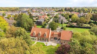 Verscholen op een prachtig perceel van maar liefst 35a 89ca ligt deze unieke villa, een eigendom die zich moeilijk laat vergelijken met het klassieke woningaanbod. Achter de poort ontvouwt zich een domein waar authentieke architectuur, royale volumes en een groene, volledig privatieve tuin naadloos in elkaar overvloeien. <br /><br />De villa werd in 1978 gebouwd door een aannemer die koos voor duurzame materialen en verfijnd vakmanschap. Vandaag is die kwaliteit nog steeds zichtbaar in de talrijke authentieke elementen die de woning haar ziel geven. Franse zandstenen bogen, een karaktervolle erker, massief eiken deuren, elegante trappen en warme parketvloeren zorgen voor een tijdloze uitstraling die doorheen de jaren met zorg werd behouden. <br /><br />Bij het binnenkomen in de hoofdwoning wordt u verwelkomd in een ruime inkomhal waar de indrukwekkende Franse zandstenen bogen meteen de toon zetten. De authentieke materialen en het rijke eiken schrijnwerk creëren een sfeer van klasse en warmte. Vanuit de inkomhal vloeit de woning verder naar de verschillende leefruimtes, bestaande uit een sfeervolle woonkamer, een gezellige eetkamer en een ruime keuken waar het dagelijkse leven zich ongetwijfeld afspeelt. Daarnaast beschikt het gelijkvloers over een bureau, ideaal voor thuiswerk of een vrij beroep, een praktische bijkeuken en extra bergruimte. <br /><br />Op de verdieping bevinden zich drie ruime slaapkamers en een badkamer. Via een zolderluik bereikt u de geïsoleerde zolder, die perfect dienst doet als extra opslagruimte. Ondergronds beschikt de woning bovendien over een kelder, wijnkelder en kruipkelder. <br /><br />Doorheen de woning zorgen de combinatie van natuursteen, massief eikenhout en parketvloeren voor een bijzonder warme sfeer. Hier voelt elke ruimte authentiek aan, zonder in te boeten aan comfort. <br /><br />Een absolute meerwaarde van deze eigendom is de volledig geïntegreerde tweede woongelegenheid. Via een charmante overdekte boogverbinding staat deze zelfstandig woonunit in contact met de hoofdwoning, terwijl beide delen toch hun eigen privacy behouden. <br /><br />Deze tweede woongelegenheid werd de afgelopen jaren grondig gemoderniseerd en straalt hedendaagse klasse uit. De lichtrijke leefruimte met open keuken vormt het centrale hart van de woning. De maatwerkkeuken met royaal kookeiland, geïntegreerde toestellen en uitgebreide kastruimte werd ontworpen met oog voor functionaliteit en esthetiek. Een elegante metalen wenteltrap leidt naar de verdieping, waar een ruime slaapkamer met ingebouwde kastenwand en een comfortabele badkamer met ligbad en aparte douche werden ingericht. <br /><br />Ook buiten onderscheidt deze eigendom zich moeiteloos. De prachtig onderhouden tuin biedt een uitzonderlijk gevoel van rust en privacy. Volwassen beplanting, uitgestrekte groenzones en verschillende terrassen zorgen ervoor dat u op elk moment van de dag een aangename plek in de zon of schaduw vindt. <br /><br />De tweede woongelegenheid beschikt over een eigen terras met zonneluifel en een afzonderlijke tuinzone. Beide tuingedeeltes worden op een sfeervolle manier met elkaar verbonden via een fontein, waardoor het geheel aanvoelt als een harmonieus privépark. <br /><br />Deze eigendom biedt een zeldzame combinatie van authentieke charme, kwalitatieve afwerking, uitzonderlijke oppervlakte en flexibele woonmogelijkheden. Een ideale thuis voor grote gezinnen, kangoeroewonen, zorgwonen of wie wonen en werken wenst te combineren in een unieke en stijlvolle omgeving.