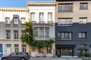 <p>Op sommige plekken in Antwerpen hoef je de locatie nauwelijks nog uit te leggen.<br />De Kloosterstraat kent iedereen. Antiek, design, kleine boetieks, koffie, restaurants en altijd wel iets te ontdekken. En net om de hoek, in de Korte Vlierstraat, staat dit karaktervolle handelshuis.<br />Een pand met 294 m² ruimte, een flinke dosis persoonlijkheid en vooral: mogelijkheden.</p>
<p>We beginnen beneden.<br />Vandaag bevindt zich hier een chocoladeatelier. En eerlijk? Dat klinkt op zich al behoorlijk goed.<br />Maar het handelsgelijkvloers hoeft uiteraard niet naar chocolade te blijven ruiken. Met zijn grote open ruimte en etalage aan de straatzijde kan je hier heel wat kanten uit. Een winkel, atelier, showroom, kantoor, praktijk, creatieve studio… Wie droomt van een eigen zaak met een sterke zichtbaarheid en een toplocatie, mag hier alvast beginnen dromen. En bovendien zijn hier 2 wc's voorzien.<br />Achteraan bevindt zich een keuken en dankzij de aparte meters kan het handelsgedeelte bovendien mooi functioneren naast het woongedeelte.</p>
<p>En dan gaan we eerst even naar de kelder.<br />Geen plek waar je tussen spinnenwebben en oude verfpotten naar de watermeter moet zoeken. Hier werden de authentieke bakstenen gewelven net uitgespeeld en kreeg de ruimte zowaar een eigen bar.<br />Een verborgen plek onder de stad, ideaal als extra ontspanningsruimte, wijnkelder of gewoon als die plek waar een avond soms iets langer duurt dan gepland.</p>
<p>Vanaf de eerste verdieping begint het privéleven.<br />En na de uitgesproken commerciële ruimte beneden verandert de sfeer hier helemaal. Een ruime leefkamer met houten vloer biedt plaats aan zowel salon als eetkamer. De open keuken is gloednieuw (2024), uitgerust met gootsteen, inductiekookplaat (4 pitten) en ingebouwde dampkap.</p>
<p>Aansluitend ligt een gezellige buitenruimte. Een groen hoekje midden in de stad om heerlijk te genieten van een tasje koffie, aperitief in de zon of gewoon vijf minuten eens helemaal niets te doen.</p>
<p>Op de 2de verdieping bevindt zich de grote slaapkamer met aparte dressing en daarnaast een ruime badkamer. En ook die past helemaal bij het karakter van het huis: een groot ligbad, aparte douche en een eigenzinnige zwart-witte vloer.</p>
<p>Helemaal boven wachten nog twee kamers.<br />Slaapkamers, hobbyruimtes,… kies maar.<br />En dan is er nog het uitzicht.<br />Want boven de daken krijg je Antwerpen er zomaar bij. Met onder andere de kathedraal aan de horizon. Niet slecht als achtergrond bij je eerste koffie van de dag.</p>
<p>De Kloosterstraat ligt letterlijk om de ene hoek, de Sint-Andriesplaats om de andere hoek. De vernieuwde Scheldekaaien en het Zuidpark zijn vlakbij en voor leuke winkels, koffie of een goed restaurant hoef je hier zelden ver te wandelen. Bovendien zijn er plannen om de straat als woonerf in te richten.</p>
<p>Dit is dan ook geen woning die zich makkelijk in één vakje laat stoppen.<br />Het is een handelspand, een woning, een werkplek en vooral een plek met karakter.</p>
<p>Troeven:<br />– toplocatie <br />– handelsgelijkvloers, huidige eigenaars zijn bereid dit te huren tegen marktconforme voorwaarden, valt zeker en vast te bespreken!<br />– aparte meters <br />– buitenruimte <br />– kelder met bar <br />– airco <br />– EPC C, inclusief 12 zonnepanelen<br />- Prachtig uitzicht</p>