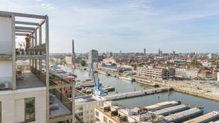 Gelegen op de 13de verdieping van het architecturale gebouw 'Pergola', bieden wij dit spectaculaire appartement te koop aan. Dit is exclusief wonen op grote hoogte in de vernieuwde, duurzame wijk De Nieuwe Dokken in Gent. Een autoluwe woonomgeving die absolute rust garandeert, terwijl het bruisende stadscentrum en alle belangrijke voorzieningen bijzonder vlot bereikbaar blijven.<br /><br />Wat dit pand werkelijk uniek maakt, zijn de weidse terrassen die de woning volledig omringen. U geniet hierdoor van een permanent, panoramisch uitzicht op de waterpartijen, de skyline en de iconische drie torens van Gent. Binnen en buiten lopen naadloos in elkaar over, waarbij de verschillende oriëntaties u op elk moment van de dag de keuze bieden tussen heerlijke zon of verfrissende schaduw.<br /><br />Via de lift stapt u in alle privacy rechtstreeks uw appartement binnen. De open leefruimte vormt het kloppend hart van de woning en sluit direct aan op het hoofdterras. In de sublieme open keuken zijn de hoogwaardige toestellen discreet weggewerkt achter elegante schuifwanden voor een uiterst strak, ordelijk en esthetisch geheel.<br /><br />Het nachtgedeelte biedt twee volwaardige slaapkamers en een kinderkamer, elk gekenmerkt door royaal binnenvallend licht. Bovendien beschikt elke kamer over een eigen, luxueus afgewerkte badkamer met kwalitatieve topmaterialen.<br /><br />Een absolute buitenkans voor wie droomt van een exclusieve woonervaring, een feilloze afwerking en sublieme zichten over Gent!<br /><br />Bestuursmaatregelen in het maatregelenregister: nee