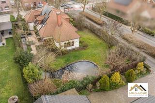 Deze stijlvolle villa bevindt zich in het groene Merelbeke. Je komt binnen via een ruime, elegante traphal die toegang biedt tot alle vertrekken op het gelijkvloers. Aan de voorzijde bevindt zich een zeer ruim bureau, ideaal voor thuiswerk of praktijkruimte. Verder is er een apart gastentoilet en een vlotte doorgang naar de leefruimtes. De volledig ingerichte keuken is uitgerust met een grote eethoek en kamerhoge ramen die zorgen voor overvloedig daglicht en een directe verbinding met de tuin. Aansluitend bevindt zich een praktische bijkeuken met ruimte voor wasmachines en extra opslag. Daarnaast is er een dubbele garage met automatische poorten, geschikt voor twee wagens en bijkomende bergruimte. De leefruimte is royaal en omvat een eetplaats met zicht op de tuin. Uniek aan deze woning is de gezellige open haardkamer met hoog plafond, die warmte en sfeer toevoegt aan het geheel. Bovendien is er een kelderruimte aanwezig, handig als extra opslag. Op de bovenverdieping leidt een stijlvolle nachthal naar vier ruime slaapkamers. De master bedroom beschikt over een comfortabele dressing met daglicht. Twee slaapkamers bieden ruim plaats aan een bed en kasten, terwijl de vierde kamer bijzonder groot is en tal van inrichtingsmogelijkheden biedt. Ook een nachttoilet is voorzien op deze verdieping. De tuin, momenteel in winterslaap, is een ware oase voor liefhebbers van groen. Dankzij de verzorgde mixborders, een sfeervolle vijver en het beschutte terras is het hier aangenaam vertoeven. Als extra troef is er in de hoek van de tuin een charmante blokhut met sauna. Deze villa combineert comfort met klasse: zonnepanelen, een ruime oprit en een luxueuze uitstraling maken het geheel compleet. Ideaal voor wie op zoek is naar een ruime, instapklare woning met karakter, privacy en hoogwaardige afwerking, in een rustige en toch vlot bereikbare omgeving. Bezoekdag: 16/05. Inschrijven via mail naar tommy@immo-home.be, geen telefonische inschrijvingen! Volg ons op Fb en Insta. Voor meer info: www.immo-home.be. GRATIS SCHATTING &amp; GRATIS FINANCIEEL ADVIES