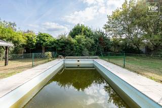 <p>In een bijzonder residentiële en groene straat, omgeven door hoogstammige bomen en verschillende kasteeldomeinen, bevindt zich deze karaktervolle villa op een zuidgericht perceel van meer dan 900 m².<br /><br />De locatie biedt een uitzonderlijk goede MOBI-score en combineert een rustige woonomgeving met een bijzonder uitgebreid aanbod aan voorzieningen. Aan de overzijde van de straat bevindt zich een apotheek. Verderop in de straat vindt u zowel Colruyt als Delhaize (open tot 20 uur, ook op zondag), een tankstation, kleinhandel en horeca. Meerdere scholen liggen op wandelafstand, terwijl de op- en afrit van de R4 op amper 2 minuten rijden bereikbaar is. Met de fiets staat u bovendien in ongeveer 12 minuten in het centrum van Gent.<br /><br />De villa beschikt over maar liefst drie slaapkamers alle drie op de verdieping op het gelijkvloers beschik je nog over 2 aparte ruimtes die je zelf nog volledig kan inrichten. De leefruimte wordt gekenmerkt door een mooie parketvloer en sluit aan op een bijzonder lichtrijke veranda, vanwaar u een aangenaam contact heeft met de tuin.<br /><br />Zowel de tuin als het zwembad zijn optimaal zuidgericht, waardoor u hier maximaal van de zon en het buitenleven kunt genieten.<br /><br />Ook praktisch heeft deze woning heel wat te bieden. Zo is er een ruime dubbele garage die aan de binnenzijde niet door een tussenwand wordt opgedeeld. Hierdoor ontstaat één grote open ruimte die niet alleen geschikt is voor meerdere wagens, maar eveneens perfect dienst kan doen als atelier of hobbyruimte.<br /><br />Een bijkomende troef is dat al het buitenschrijnwerk recent werd vernieuwd.<br /><br />De villa is aan renovatie toe, maar vormt dankzij haar karakter, royale perceel, vijf slaapkamers, zuidgerichte tuin met zwembad, lichtrijke veranda en bijzonder ruime garage een uitstekende basis voor wie een karaktervolle woning naar eigen smaak wil afwerken.<br /><br />Een eigendom die rust en groen combineert met een uitstekende bereikbaarheid en de nabijheid van alle dagelijkse voorzieningen.<br /><br />Het perceel van de villa en het aanpalende bouwperceel dienen na afloop van de biedingsronde en de toewijzing aan de uiteindelijke koper nog officieel te worden opgesplitst alvorens de notariële akte kan worden verleden. De verkoop gebeurt bijgevolg via een aankoop-verkoopbelofte, onder de opschortende voorwaarde van de opsplitsing van beide percelen.</p>