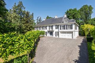<p><strong>Deze uitzonderlijke villa is gelegen op een perceel van ca. 4.950 m² langs de Antwerpsesteenweg in Vosselaar en combineert aanzienlijke volumes met een doordachte indeling. De royale inkomhal biedt toegang tot de leefruimtes, bestaande uit een eet- en zithoek, een afzonderlijke tv-kamer en een bureauruimte. Centraal bevindt zich de vernieuwde keuken met Gaggenau-toestellen, uitgevend op het overdekte binnenzwembad, een lichtrijke leefruimte met tuincontact en een wellnessgedeelte met sauna. Verder beschikt de woning over een inpandig duplex appartement met eigen ingang, een totaal van acht slaapkamers en zes badkamers. </strong><br /><br /><strong><span>Indeling</span><br /></strong>Via de imposante entreehal betreedt u de woning. Aan de linkerzijde bevindt zich een eerste leefruimte die is ingericht met eet- en zitgelegenheid. Aansluitend volgt een afzonderlijke tv-kamer, met daarnaast een bijkomende ruimte die zich leent tot gebruik als bureau of werkkamer.</p>
<p>Het hart van de villa is de keuken, welke zich centraal in de villa bevindt. De keuken werd enkele jaren geleden vernieuwd en is uitgerust met kwalitatieve Gaggenau-toestellen. De keuken kijkt uit op het overdekte binnenzwembad en op een aangrenzende, lichtrijke ruimte met glazen dak, ingericht als eet/leefruimte en in direct contact met de tuin. De keuken alsook de ruimte met binnenzwembad verlenen toegang tot de kelderverdieping. Deze heeft een gedeeltelijke barfunctie en een wellnessfunctie, compleet met sauna en douches.</p>
<p>Verder op het gelijkvloers bevinden zich een vestiaire, een gastentoilet en een wasplaats. Vanuit de wasplaats is er toegang tot de ruime garage, voorzien van meerdere poorten aan voor- en achterzijde.<br /><br /><strong><span>Verdieping</span></strong><br />Op de eerste verdieping, dewelke we bereiken via de royale wenteltrap, bevinden zich drie slaapkamers, elk met bijhorende badkamer. De mastersuite, met royale afmetingen, is uitgerust met twee dressings. De tweede verdieping omvat nog twee bijkomende slaapkamers, een speelkamer, een extra badkamer en zolderruimte.<br /><br /><strong><span>Appartement</span></strong><br />In het pand is tevens een volwaardig inpandig appartement ondergebracht, opgevat als duplex en geschikt voor conciërge of inwonende ondersteuning. Dit appartement beschikt over een leefruimte, keuken, 2 badkamers en 3 slaapkamers, en functioneert autonoom binnen het geheel met eigen ingang.</p>
<p>De villa beschikt in totaal over 8 slaapkamers en 6 badkamers, en biedt een bewoonbare oppervlakte van ca. 1.436 m² (inclusief appartement). Het geheel wordt omgeven door een ruim, groen perceel dat privacy en rust waarborgt, met behoud van een vlotte bereikbaarheid.</p>
<p>Een eigendom met aanzienlijke volumes en diverse gebruiksmogelijkheden, geschikt voor wie ruimte, comfort en een zekere autonomie binnen het wonen weet te waarderen. Verder biedt de woning nog de mogelijkheid voor andere invullingen, zoals bv. B&B, kleinschalig restaurant, kantoor (bv. private banking) of een andere, rustige, zelfstandige activiteit.<br /><br /><span><strong>Bijzonderheden:</strong></span><br />- Riant perceel van ca. 4950m<span>²</span><br />- Totaliteit van 8 slaapkamers en 6 badkamers<br />- Indoor zwembad met welness<br />- Royale ruimtes met doordachte indeling<br />- Gunstige ligging nabij invalswegen en vlotte bereikbaarheid naar zowel Nederland als Antwerpen.</p>