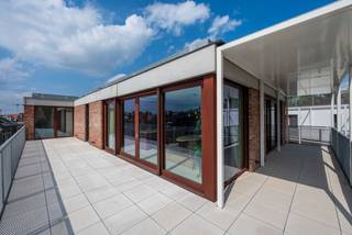 <p>Au sein du superbe projet Portier 51, qui compte 22 appartements, se trouve un penthouse sublime offrant une vue phénoménale sur l'église Notre-Dame-sur-la-Dyle et sur l'élégante maison de concierge, récemment rénovée. L'immense terrasse en forme de L qui entoure l'appartement à l'est et au sud est tout simplement impressionnante. Les finitions soignées et les matériaux haut de gamme utilisés dans ce magnifique appartement sont un véritable régal pour les yeux. Ici, vous vous sentirez vraiment chez vous et pourrez vivre en toute tranquillité au cœur de Malines, à proximité des commerces, des terrasses les plus conviviales, des bars et des restaurants, dans une rue calme et peu fréquentée. Tout est accessible à pied ou à vélo, tandis que la voiture peut être garée confortablement sous le site (moyennant un achat supplémentaire).</p>
<p>AGENCEMENT :</p>
<p>L'appartement est divisé par un vaste hall d'entrée en une aile jour et une aile nuit.</p>
<p>Une porte pivotante en acier donne accès à l’agréable pièce à vivre avec cuisine ouverte, où une magnifique lumière pénètre par les grandes baies vitrées coulissantes en bois. Un superbe îlot de cuisine en noyer avec un plan de travail en pierre naturelle attire tous les regards dans la pièce. La cuisine SieMatic est équipée d’appareils électroménagers haut de gamme de la marque Miele (four à vapeur combiné, four multifonction, réfrigérateur, plaque à induction avec hotte intégrée, lave-vaisselle). Un débarras (technique) très pratique est dissimulé derrière le mur sur mesure. Sur la droite se trouve le bureau avec des étagères, un plan de travail et une armoire de rangement. Grâce à l’utilisation systématique de matériaux haut de gamme, l’ensemble forme un tout harmonieux sur le plan visuel dans tout l’espace de vie. Il y a suffisamment de place pour une grande table et un coin salon confortable. La grande terrasse – en partie couverte – entoure tout l’espace de vie, qui se prolonge ainsi naturellement vers l’extérieur.<br /><br />Une première salle de bains en mortex, dotée des mêmes meubles en noyer et d’un plan de travail en pierre naturelle, est équipée d’un lavabo, de toilettes et d’une douche à l’italienne. Les élégants détails en bronze brossé lui confèrent une allure luxueuse.<br /><br />Près du hall d’entrée se trouvent les toilettes pour invités avec un lavabo. Derrière celles-ci se trouve un deuxième débarras pouvant servir de buanderie.<br /><br />De ce côté se trouvent les 3 chambres, dont la chambre parentale dispose également d’une salle de bains « en suite » entièrement dans le même style que l’autre, avec double lavabo et douche à l’italienne.<br /><br />PRATIQUE :<br /><br />Entièrement conforme aux dernières normes de durabilité : pompe à chaleur géothermique et air-eau, panneaux solaires, isolation, refroidissement passif, système de ventilation D+.<br /><br />Indice énergétique E19. Votre consommation d’énergie est ainsi réduite au minimum. Cela vous permet également d'être exonéré de la taxe foncière pendant 5 ans.<br /><br />Un local à vélos commun est à votre disposition.<br /><br />Le site dispose d’un jardin intérieur élégamment aménagé qui fait référence à l’ancien jardin du couvent. Il est fermé par des portails en bois. Partout, des matériaux de qualité ont été utilisés et les finitions sont soignées, jusque dans les moindres détails, des escaliers dotés de balustrades modernes en bois à la signalisation originale des étages.<br /><br />Charges communes : 295 euros/mois.<br /><br />Il est disponible immédiatement.<br /><br />Le penthouse peut être acheté au taux de TVA de 6 % si les conditions sont remplies.<br /><br />Une place de parking sous le site peut être acquise au prix de 38 000 euros hors TVA.<br /><br />Ce magnifique bien vous intéresse et vous souhaitez le visiter ? N'hésitez pas à contacter Tinne Schotsmans : 0477 60 21 99 ou tinne.schotsmans@quares-trevi.be</p>