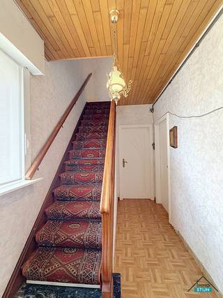Deze ruime woning geniet van een vlotte verbinding met de E403 en het openbaar vervoer en ligt bovendien in de nabijheid van diverse winkels. Via de inkomhal bereik je de lichtrijke woonkamer, de keuken en de eerste verdieping. De woonkamer biedt voldoende plaats voor een gezellig zitgedeelte en een eetkamer. De naastgelegen keuken is ingericht met een geïnstalleerde keuken en geeft toegang tot de kelder en een tweede woonkamer. Vanuit deze tweede woonkamer bereik je de wasberging met aansluitend een badkamer, voorzien van een douche en lavabomeubel. Via de hal kom je bij het afzonderlijke toilet. Op de eerste verdieping bevinden zich de nachthal, een tweede badkamer en drie slaapkamers. Deze badkamer is uitgerust met een ligbad, lavabo en toilet. Mits het opnieuw plaatsen van een vaste trap kan ook de tweede verdieping opnieuw volwaardig worden benut. Hier werden nog twee extra slaapkamers ingericht. Naast de woning loopt een oprit met poort die toegang geeft tot de ruime garage en de tuin. Buiten is er bovendien een kleine werkplaats, ideaal voor wie graag klust of extra bergruimte zoekt. Achteraan de tuin bevinden zich nog een moestuin en een kippenhok. Een ruime woning met heel wat mogelijkheden, zowel binnen als buiten. (sted.inl.: in aanvraag)
