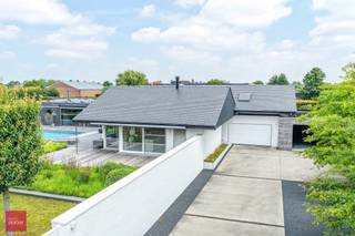Afgeschermd van straatbeeld en met toegangsdreef bereikbaar. Ruime tijdloos hernieuwde villa (462m² vloeroppervlakte) bestaande uit een inkomhall, living met open haard, ingerichte keuken (Fraeye), eetruimte, annex berging met toegang tot mooie kelder en zolder, 3 slaapkamers (1 beneden), badkamer en bureel op verdieping. Aangesloten uitbouw met hoofdslaapkamer / dressing, / badkamer, leefruimte met open haard, sauna, ontspanningsruimte, technische ruimte. Garage voor 2 wagens, carport met tuinberging en parking. Zwembad (Bob Monteyne) met buitendouche. Alle modern comfort (vloerverwarming, 59m² zonnepanelen met groenestroomcertificaten tot 2032, 20.000 l regenwater etc)