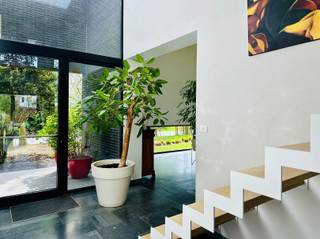 Deze exclusieve, moderne woning (bouwjaar 2010) combineert hoogwaardige afwerking met een uitzonderlijk gevoel van ruimte en licht. Dankzij de hoge plafonds, grote raampartijen en doordachte architectuur geniet u hier van een unieke woonbeleving. Bovendien is de woning volledig instapklaar.U betreedt de woning via een stijlvolle glazen deur die uitgeeft op een indrukwekkende inkomhal met extra hoog plafond. Hier bevinden zich een gastentoilet met handenwasser en een ingemaakte vestiairekast.De leefruimte vormt het absolute pronkstuk van de woning. De uitzonderlijke plafondhoogte en de naadloze overgang naar het overdekte terras creëren een luxueus gevoel. Dankzij de doorlopende vloer vloeien binnen- en buitenruimte harmonieus in elkaar over, ideaal voor wie houdt van openheid en licht. De volledig geïnstalleerde keuken is uitgerust met kwalitatieve toestellen en sluit perfect aan op de leefruimte. Aansluitend vindt u een praktische bergruimte met rechtstreekse toegang tot de tuin en de dubbele inpandige garage. De aangelegde tuin is een oase van rust en privacy, waar u in alle comfort kan genieten van het groen, gezellige diners of zonnige dagen. Op de eerste verdieping zorgt de strakke nachthal voor een elegant en open karakter. De master bedroom biedt een prachtig zicht op de tuin en wordt aangevuld met een dressing. Verder beschikt de woning over een luxueus ingerichte badkamer en een tweede volwaardige slaapkamer. Op de nachthal is er bovendien ruimte voorzien voor een bureauhoek of thuiswerkplek.Deze woning is de perfecte combinatie van design, comfort en functionaliteit, en biedt alles wat u mag verwachten van hedendaags wonen op topniveau.Interesse? Aarzel dan zeker niet ons te contacteren. Tot snel! (G-score: A/ P-score/ D)