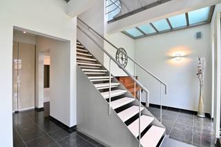 In een rustige doodlopende straat, op een uiterst centrale ligging nabij de N3 en N80 richting Tienen, Alken en omliggende gemeenten, bevindt zich deze uitzonderlijk knappe villawoning met een tijdloze architectuur en een hoogstaand afwerkingsniveau. Scholen, winkels, de Grote Markt, het LAGO-zwembad en tal van wandel- en fietsroutes bevinden zich op korte afstand, wat deze locatie niet alleen uiterst toegankelijk maar ook bijzonder kindvriendelijk maakt.<br /><br />Deze stijlvolle villa werd gebouwd in 1999/2000 volgens een vooruitstrevend architecturaal concept en werd doorheen de jaren met de grootste zorg onderhouden en verder gemoderniseerd naar hedendaagse normen. De combinatie van kwalitatieve materialen, royale volumes en overvloedige lichtinval zorgt voor een unieke woonbeleving waar comfort en elegantie perfect samenkomen.<br /><br />Via de ruime inkomhal met vestiaire en apart gastentoilet betreedt u een woning die meteen indruk maakt door haar openheid en licht. De inkomhal vormt het centrale hart van de woning en biedt bovendien ruimte voor een bureel of stijlvolle ontvangstruimte. De royale leefruimte met gezellige zithoek, eetkamer en leeshoek sluit naadloos aan op de open leefkeuken. Dankzij de vele grote raampartijen geniet elke ruimte van een prachtige connectie met de tuin en een overvloed aan natuurlijk licht. De volledig uitgeruste keuken beschikt over kwalitatieve toestellen van onder andere Electrolux (inductiekookplaat, microgolfoven, heteluchtoven), Miele (afwasmachine), AEG (koelkast) en NOVY (dampkap), afgewerkt met een elegant natuurstenen werkblad, dubbele spoelbak met afdruipzone en tal van praktische ingewerkte voorzieningen zoals diverse stopcontacten. Verder omvat het gelijkvloers een praktische wasplaats met toegang tot de tuin, veel maatwerkkasten en een ruime inpandige garage met zijdelingse ingang naar de carport.<br /><br />Op de verdieping creëert de mezzanine een prachtig ruimtelijk gevoel. Hier bevinden zich drie volwaardige slaapkamers, een aparte douchekamer, een afzonderlijk toilet én een luxueuze master suite met walk-in dressing en stijlvolle badkamer met ligbad.<br /><br />Ook de volledig ingerichte kelderverdieping biedt verrassend veel extra leefruimte en mogelijkheden. Hier vindt u onder andere een fitnessruimte, ontspanningsruimte, extra salon, technische ruimte, een kelderberging en een koude opslagruimte.<br /><br />Buiten geniet u van een volledig aangelegd en omheind perceel met een prachtig aangelegde, zuid geörienteerde tuin. Het ruime terras, de sfeervolle vijver, het tuinhuis en de verzorgde beplanting creëren een oase van rust en privacy. Extra troef is de bijkomende carport naast de woning.<br /><br />Bent u op zoek naar een instapklare villa met uitstraling, ruimte, luxe en een topligging? Aarzel dan niet en bel ons snel op 011 70 70 19 voor een afspraak.