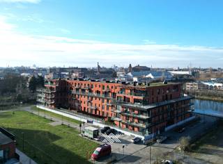 Dit lichtrijk gelijkvloers appartement maakt deel uit van de succesvolle ontwikkeling <em>København</em>. Deze residentie bevindt zich in een wijk die volop in ontwikkeling is en gekenmerkt wordt door nieuwe projecten met een duidelijke opwaardering van de omgeving. Een ligging die het beste van beide werelden combineert: de rust van de Voorhaven en de nabijheid van het stadsleven met vlotte ontsluiting naar de R4 en R40. <br /><br />Het tweeslaapkamer appartement heeft een bewoonbare oppervlakte van 94 m<sup>2</sup> en biedt een zonnig zuidoostelijk gericht terras van liefst 25,8 m<sup>2</sup>. De indeling is als volgt: een inkomhal, een lichtrijke leefruimte ingedeeld in een eet- en zitplaats met rechtstreekse toegang tot het terras en een open keuken. Via de nachthal heeft men toegang tot het toilet, de praktische berging, twee slaapkamers, met beiden toegang tot het terras, en een badkamer voorzien van een inloopdouche en dubbele lavabo.<br /><br />Tot slot dient bij dit appartement een ondergrondse autostaanplaats aangekocht te worden (€ 30.000) en kan men tevens gebruik maken van de gemeenschappelijke fietsenstalling. Het appartement wordt sinds 2024 vlot verhuurd aan een trouwe en correct betalende huurder (€ 1.100/ maand + € 85 provisie gemene lasten). Het appartement wordt verwarmd met radiatoren op aardgas voor een aangename warmte. Daarnaast is het appartement uitgerust met een ventilatiesysteem type C, wat zorgt voor een gezond binnenklimaat.