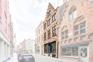 <p>In de Hoogstraat, één van de meest karaktervolle straten van Brugge, vinden we deze charmante en veelzijdige woning met een bijzondere historische uitstraling. De woning is beschermd als erfgoed en combineert authentieke elementen met hedendaags comfort. Met een <strong>EPC-label B</strong>, een <strong>conforme elektrische installatie</strong> en <strong>gasverwarming</strong> beschikt de woning bovendien over een aantal belangrijke technische troeven.</p>

<p>Via de inkomhal betreedt u de woning. Op het gelijkvloers bevinden zich een aparte bureauruimte, een praktische berging/wasruimte en een aangename stadstuin, een bijzonder mooie troef in het centrum van Brugge. Daarnaast beschikt de woning over een droge kelder, ideaal als extra bergruimte.</p>

<p>Op de eerste verdieping bevinden zich de <strong>keuken, woonkamer en een eerste slaapkamer</strong>. De tweede verdieping omvat <strong>twee ruime slaapkamers</strong>, waarbij elke slaapkamer beschikt over een <strong>eigen badkamer</strong>. Op de derde verdieping bevindt zich nog een ruime zolderverdieping, die tal van mogelijkheden biedt naargelang de wensen van de nieuwe eigenaar.</p>

<p>Dankzij de indeling, de drie slaapkamers, de twee badkamers, de zolderruimte en de buitenruimte is deze woning geschikt als karaktervolle gezinswoning, tweede verblijf of als interessante opportuniteit voor investeerders.</p>

<p><strong>Een bijkomende troef voor investeerders:</strong> de woning was in het verleden vergund voor gebruik als <strong>Airbnb</strong>. De mogelijkheden om dit concept opnieuw te activeren kunnen bijgevolg opnieuw worden onderzocht, uiteraard onder voorbehoud van de huidige regelgeving en de vereiste vergunningen.</p>

<p> </p>