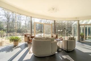 <p>Wonen in harmonie met de natuur. Deze unieke, recent geactualiseerde woning is ontworpen om het prachtige bosgebied en de vijver naadloos te integreren in uw dagelijks leven. Met een overvloed aan natuurlijk licht en vier comfortabele slaapkamers biedt deze woning een oase van rust en sereniteit. Ontsnap aan de drukte en omarm de schoonheid van uw eigen privédomein.<br /><br />De woning is ontworpen door het gekende Architectenbureau Luc Denis uit Antwerpen. De natuurlijke vijver en het omringende bos was voor de architect aanleiding een hoofverblijf met een ronde vorm te creëren met daaraan een rechthoekige uitbouw met de ruimtes die aanvullend aan de woonfunctie zijn. <br /><br />De woning is toegankelijk via de centrale inkomhal. De inkomhal is voorzien van een spiltrap uitgevoerd met transparante treden. Door de dakkoepel in het zinken dak treedt het licht hier op een subtiele manier binnen. Aan de rechterzijde de eerste kamer. Oorspronkelijk ontworpen als atelier maar uitstekend bruikbaar als slaapkamer of thuiskantoor. Deze ruimte heeft een eigen uitgang naar buiten. Daarnaast een vestiairekast, toegang tot het gastentoilet en de kelder.<br /><br />De kelder is via een vaste trap bereikbaar. In de kelder, met een oppervlakte van ca. 24m², de nutsvoorzieningen en de omvormer met batterijen voor de zonnenstroominstallatie.<br /><br />De trap geeft toegang tot de cirkelvormige verdieping. Op de verdieping 2 badkamers, 3 ruime slaapkamers en een ruime was-, en strijkruimte. De badkamers voorzien van toilet en inloopdouche. De hoofdbadkamer voorzien van een zogenaamd Japans toilet.<br /><br />Terug naar het gelijkvloers. Via de glazen deur toegang tot de leefruimte met eethoek, zithoek en tv-hoek. Totaal oppervlakte ca. 70m². Aansluitend de veranda met een oppervlakte van ca. 21m². De veranda is door een glaspartij afgesloten van de tv-hoek en heeft volledig zicht over de vijver en het achterliggende bos. De tv-hoek kent een hoofdzakelijk dichte wand waardoor een besloten sfeer wordt gecreëerd, De zithoek kijkt uit over het houten terras en de vijver naar het achterliggende bos. De waardevolle moerascipres (Taxodium distichum) is een parel aan de rand van de vijver en geeft in de zomer een aangename filtering van de zon met behoud van het licht. Aan de zithoek de eethoek en aansluitend de keuken. <br /><br />De eethoek meet ca. 24m², de keuken is volledig nieuw en heeft een moderne uitstraling. Vanuit de keuken toegang tot 2 bergingen van ca. 6 en 12m². In de achterste berging bevindt zich ook de verwarmingsinstallatie. De woning wordt verwarmd door middel van een condenserende HR-ketel op gas en heeft op het gehele gelijkvloers vloerverwarming. Terug naar de keuken toegang tot de extra badkamer met toilet en de deur naar de dubbele carport. De carport heeft een oppervlakte van ca. 36m². De woning is voorzien van een centraal stofafzuigsysteem.<br /><br />Op het dak 29 zonnepanelen van elk 405Wp geplaatst in 4 strings voor maximale opbrengst. De zonnepanelen gekoppeld aan 6 accu’s met een totale opslagcapaciteit van 20kWh. Aan de carportzijde is een laadpaal geplaatst voor het opladen van de elektrische wagens. De EPC-waarde is een uitstekende waarde voor de woning maar is nog niet aangepast met deze wijzigingen en de woning zal dus nog een stuk beter resultaat laten zien.<br /><br />Recent is er een extra overkapping gebouwd met een oppervlakte van ca. 33m². Vanaf de veranda is de woning voorzien van een houten terras met aansluitend een loopbrug. In de tuin wordt op korte termijn nog een complete louncheruimte opgericht.</p>
<p>De tuin en de vijver zijn goed onderhouden en de woning is instapkaart. Benieuwd naar deze bijzondere woning in de groene en rustgevende omgeving van Kalmthout? Bel gerust voor een uitgebreid bezoek. Via 03 240 11 99 is een afspraak snel gemaakt.</p>